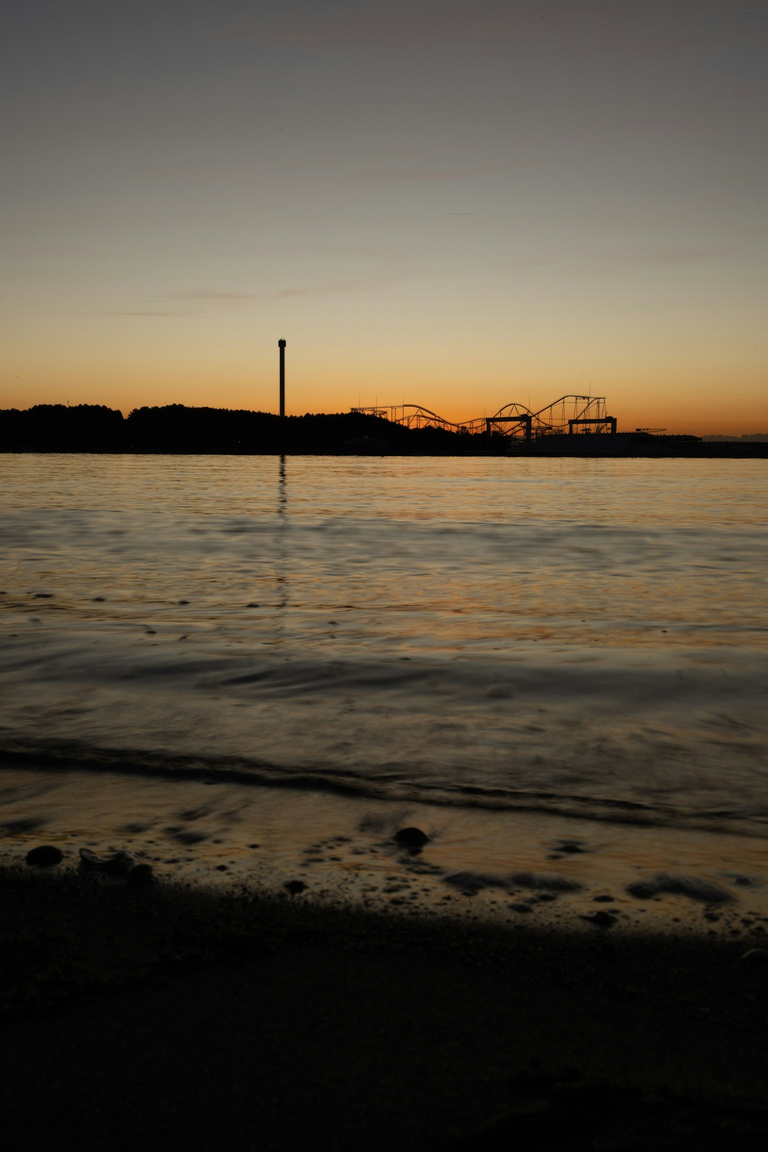 Vue de coucher de soleil côtier avec vagues et silhouette de parc d'attractions