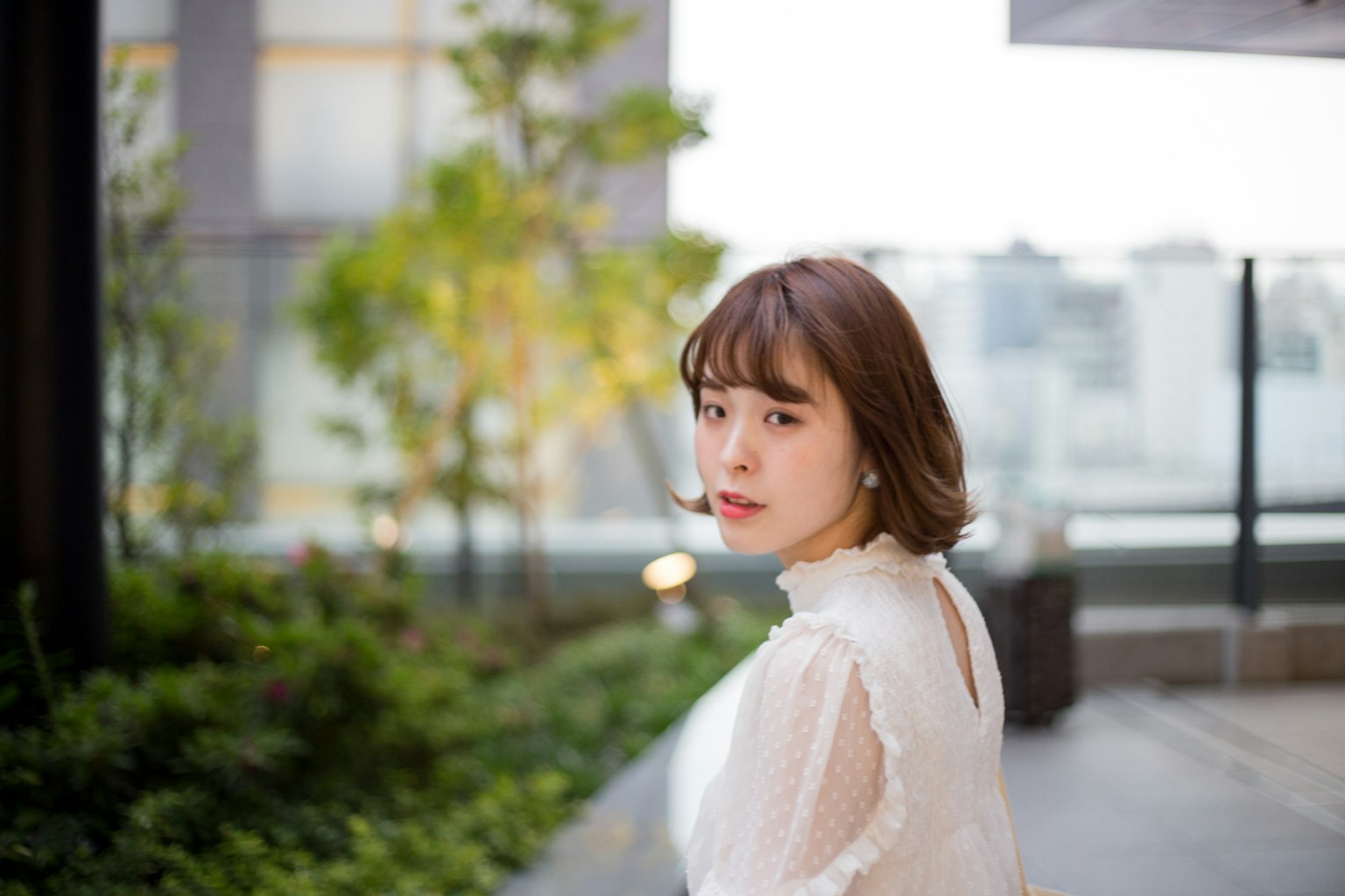 A woman in a white dress looking back with a vibrant green and urban background