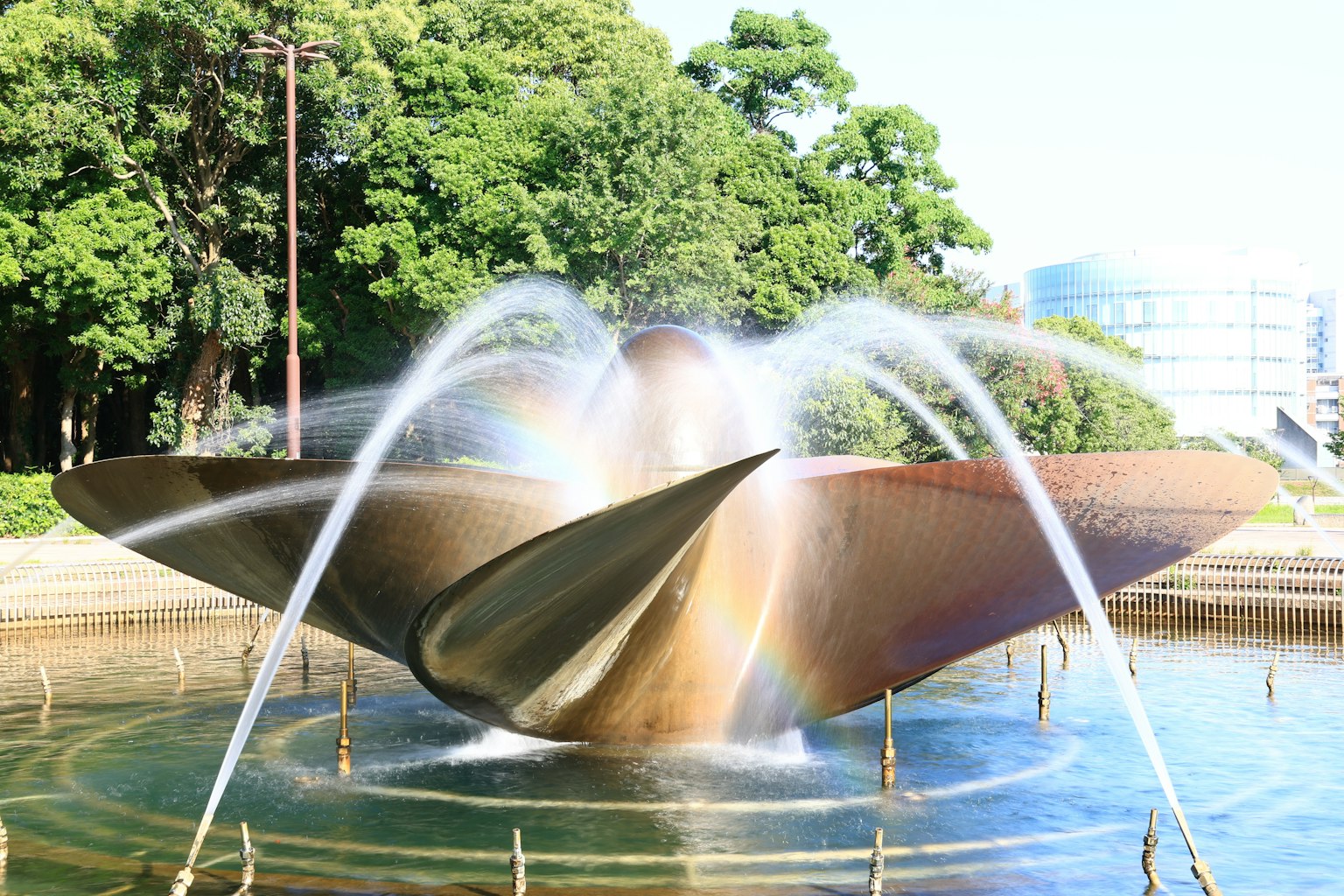 Ein schöner metallischer Brunnen im Zentrum eines Parks mit fließendem Wasser und umgebenden grünen Bäumen