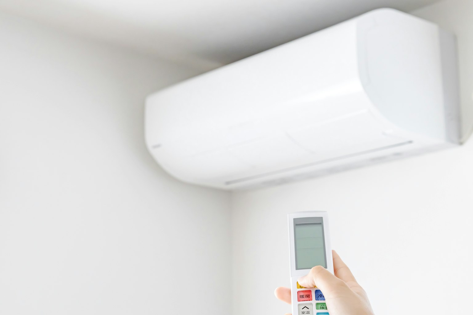 A white air conditioner mounted on the wall with a hand holding a remote control