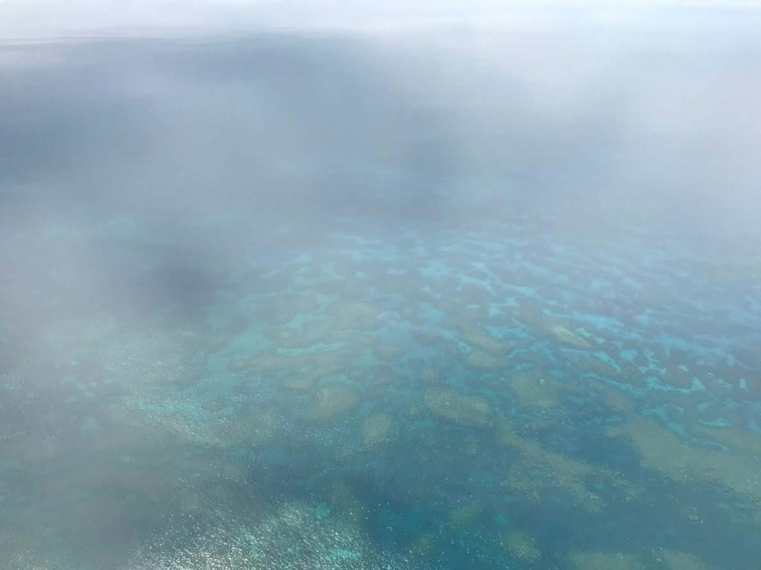 Vista aérea de arrecifes de coral parcialmente cubiertos por la niebla