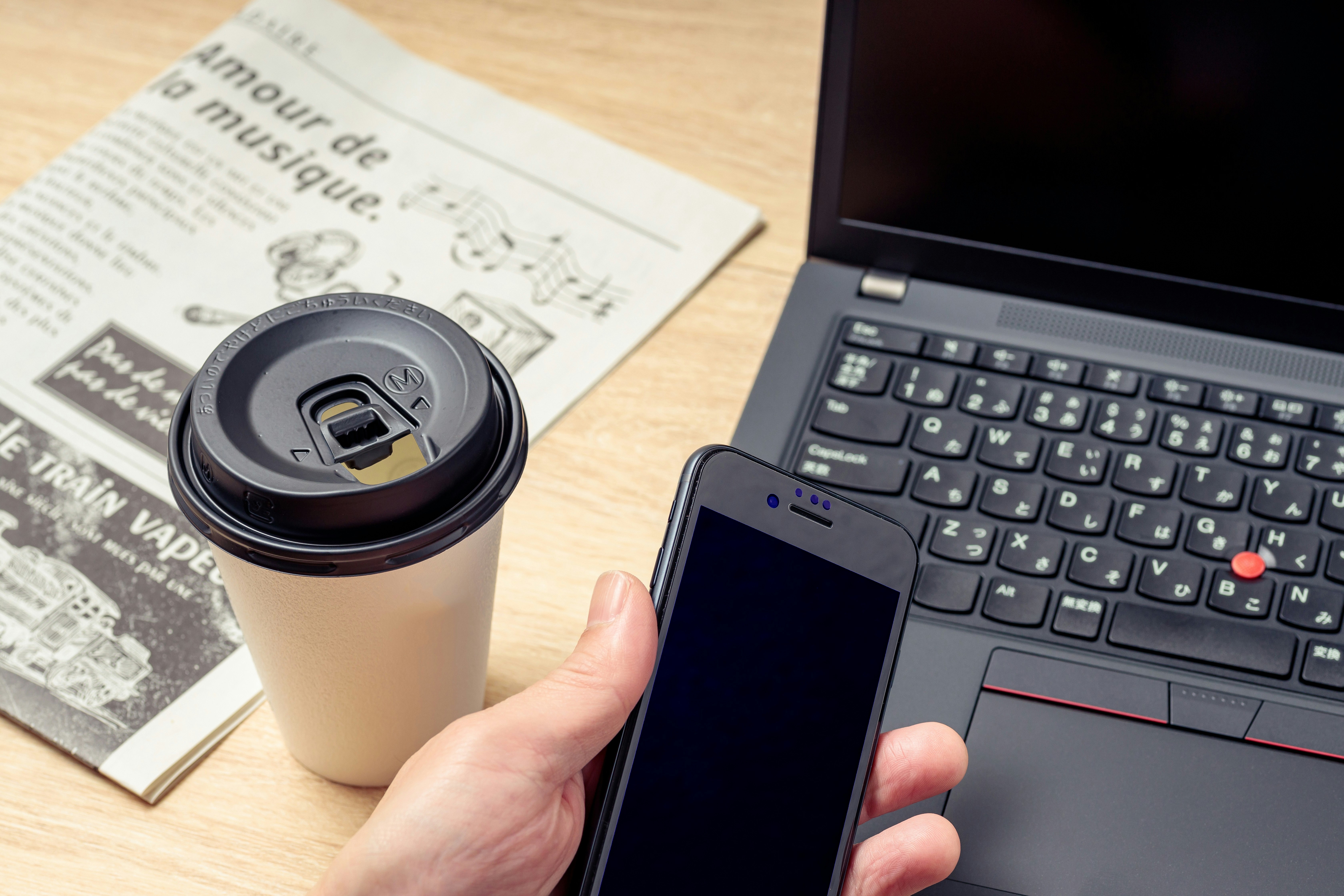 ビジネスデスクでコーヒーと新聞、PCとスマホを手にする手元