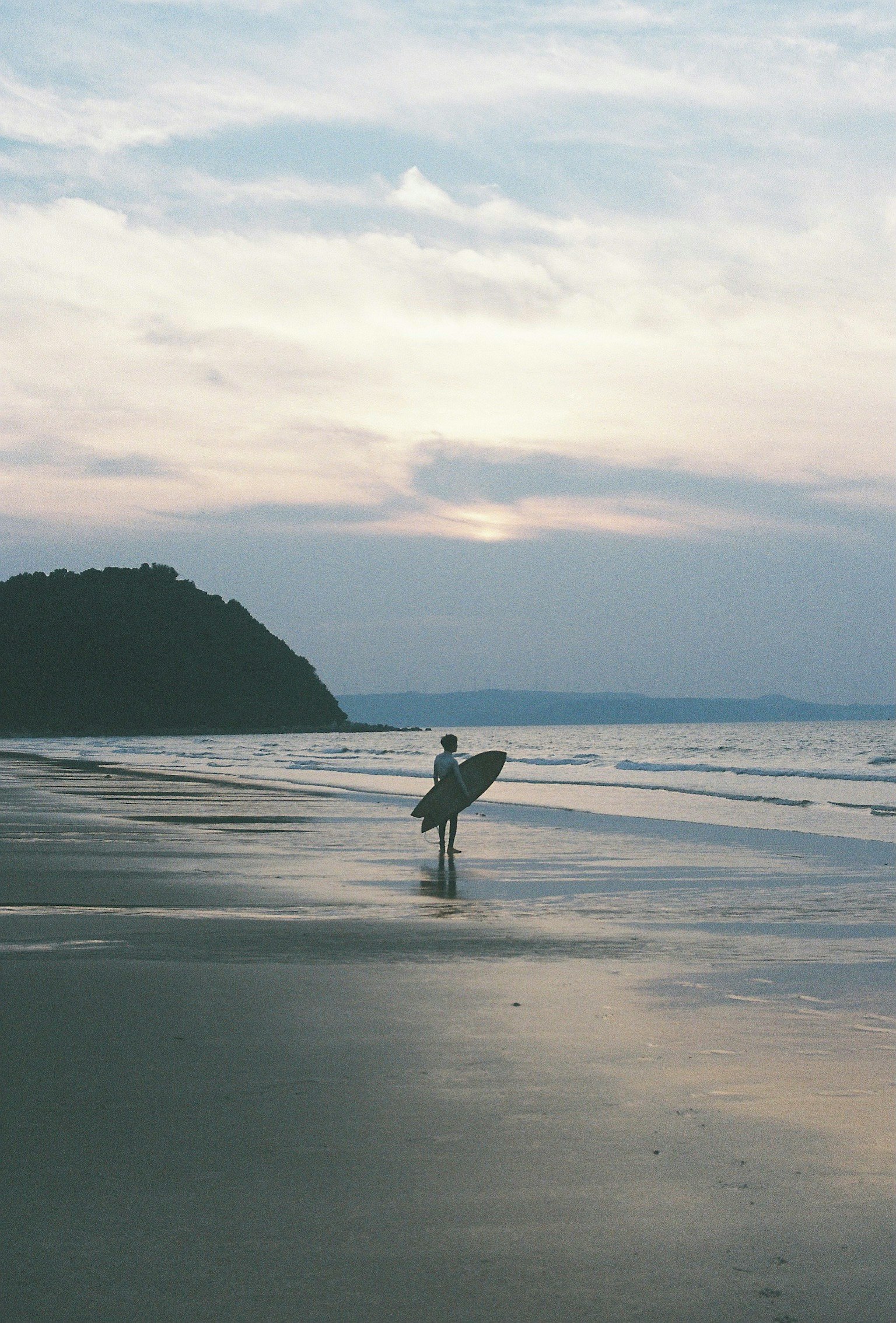 Silueta de un surfista sosteniendo una tabla de surf en la playa mar tranquilo y suaves colores del atardecer