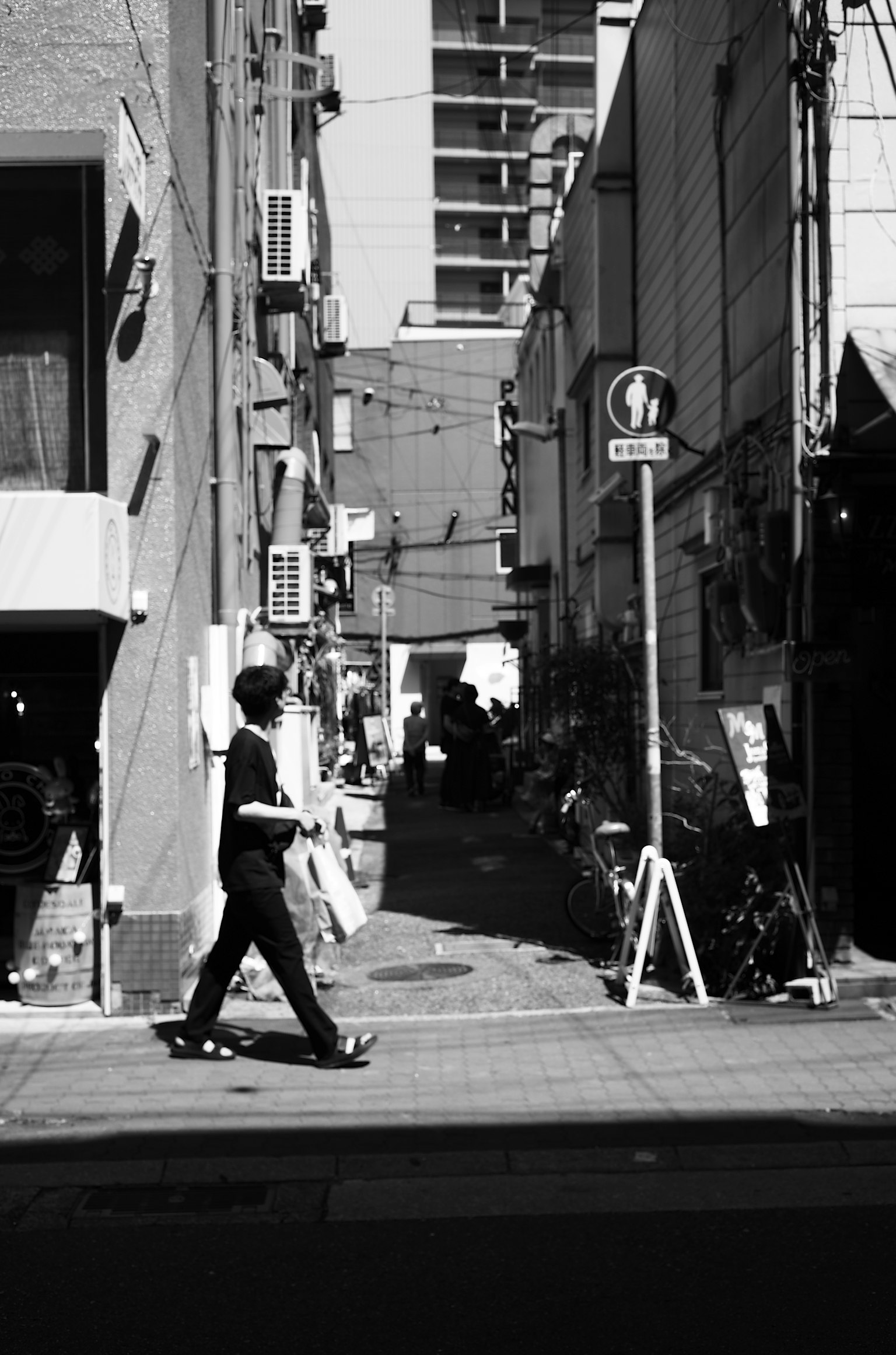 Una persona caminando en una esquina de calle en blanco y negro con un callejón estrecho