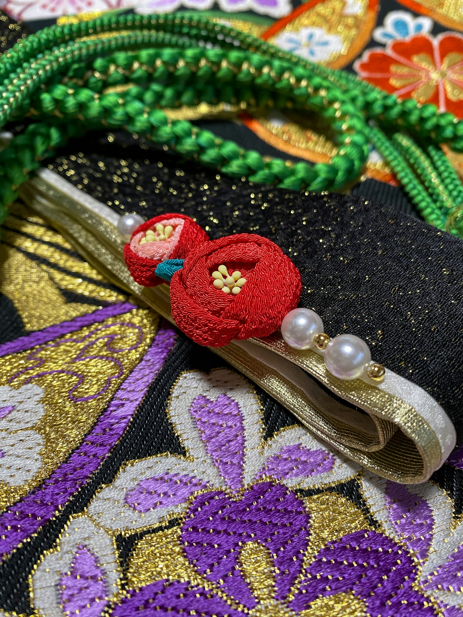 A decorative obi featuring red flower embellishments and pearls on a colorful kimono background