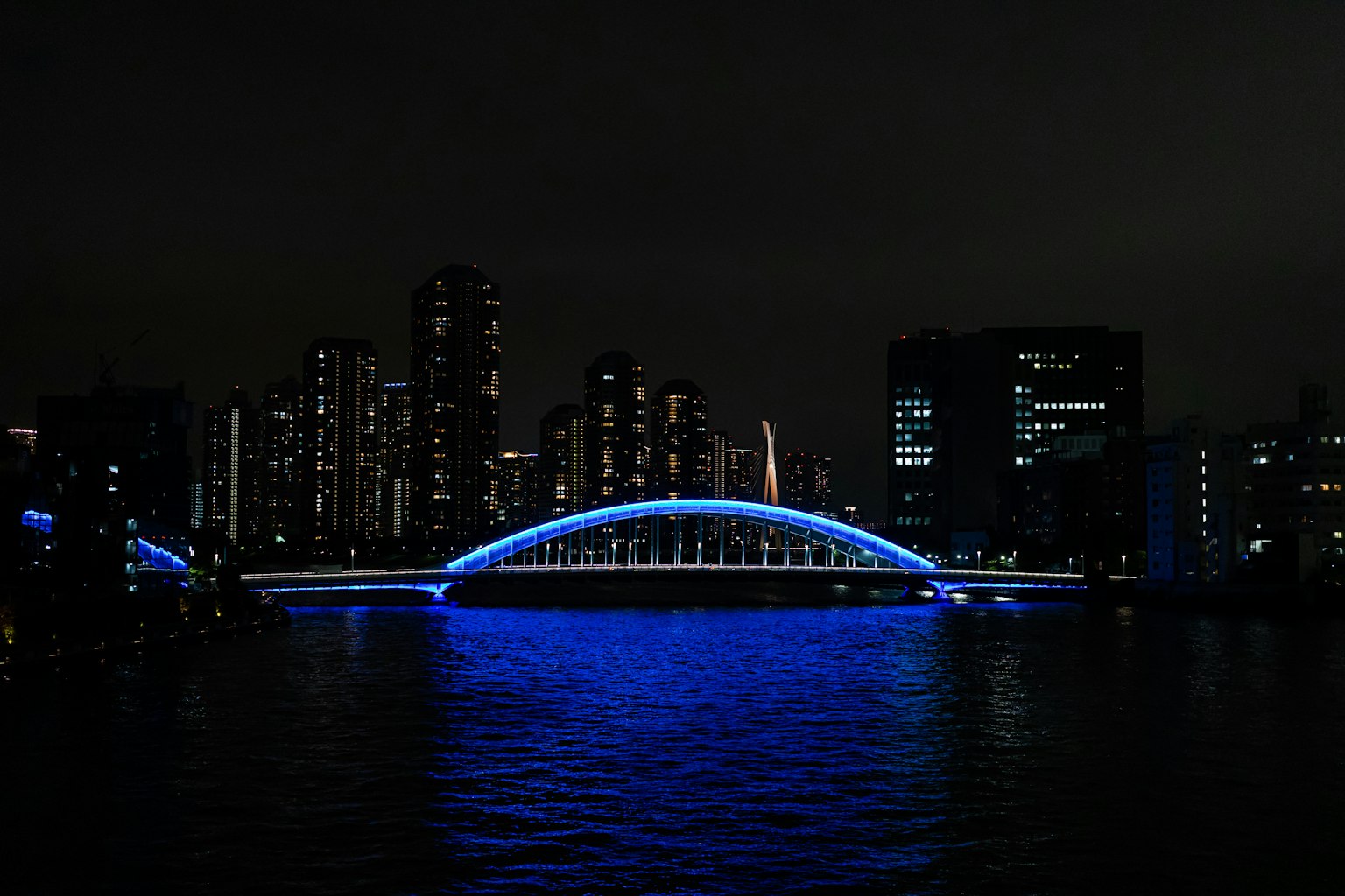 Bogenbrücke mit blauen Lichtern über einem Fluss und Stadtansicht bei Nacht