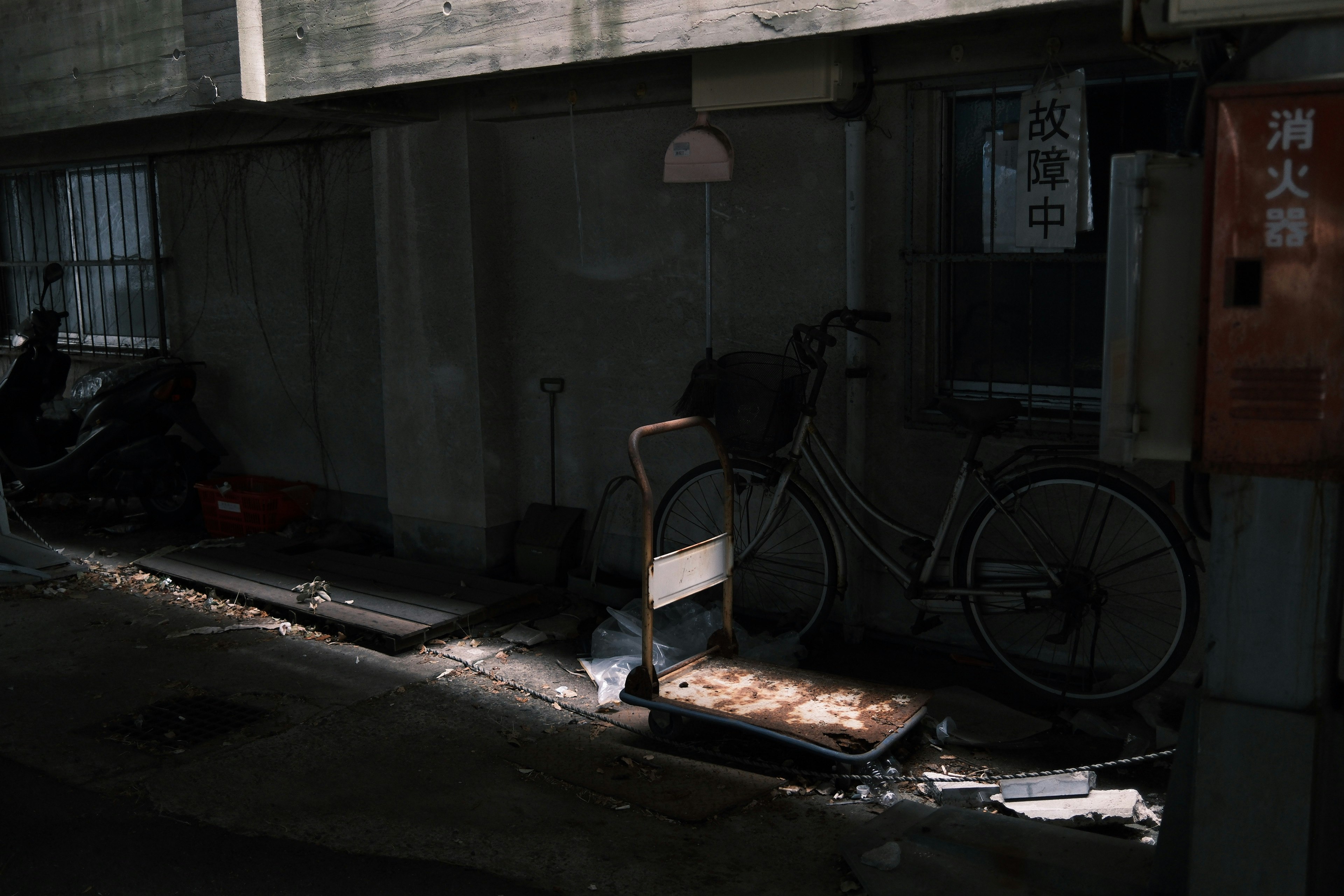 路地の壁際に置かれた自転車と傘のある薄暗い店先