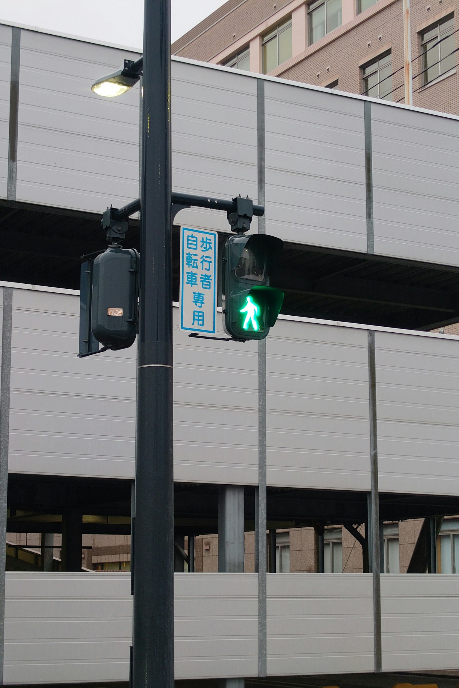 Sinyal pejalan kaki hijau ditampilkan pada lampu lalu lintas dengan fasad gedung