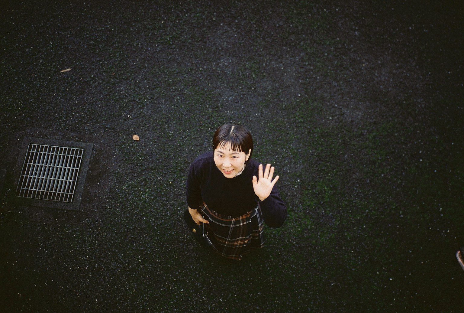 上から見下ろした女性が手を振っている写真 黒い地面とグレーのスカート