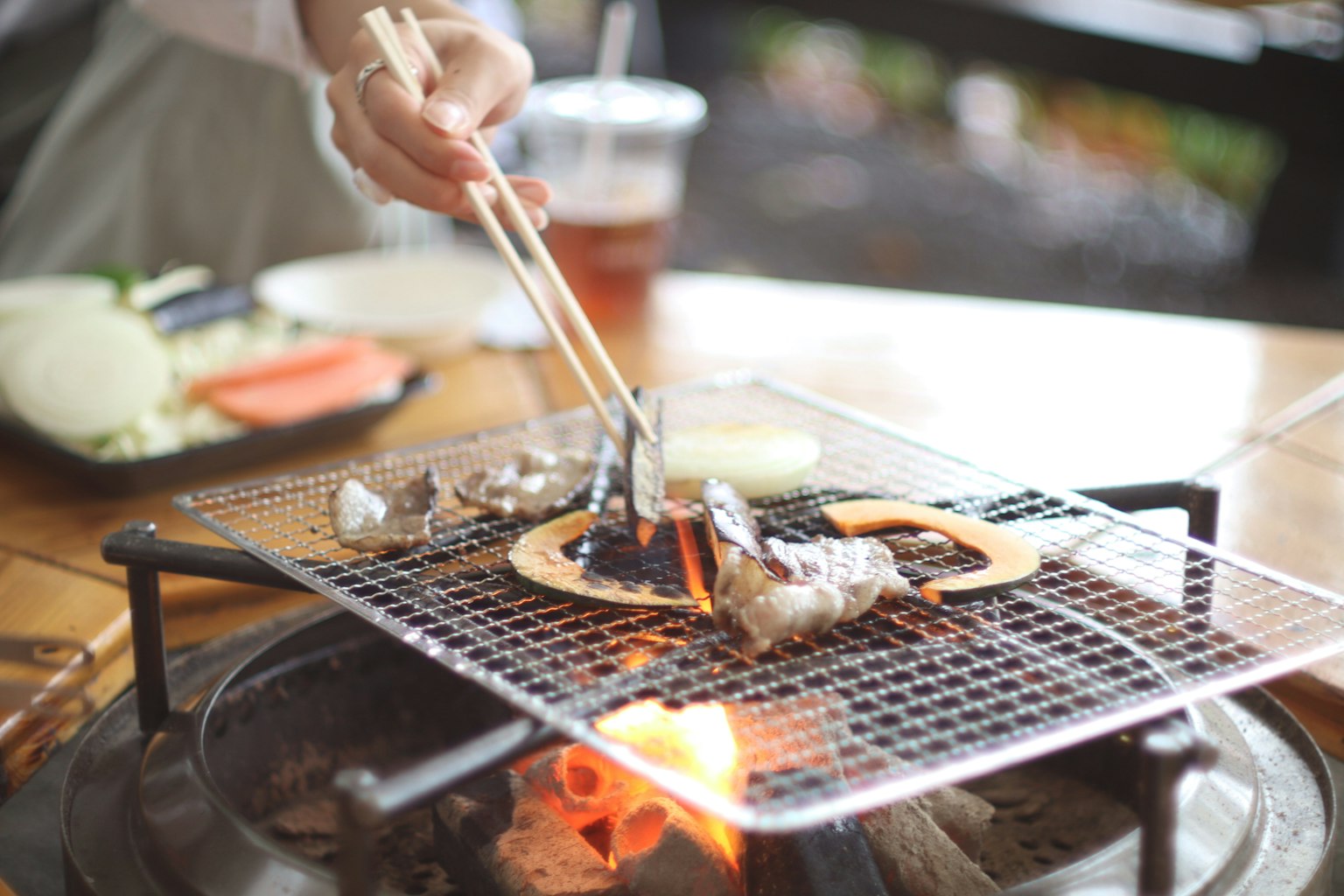 焼き網の上で焼かれている海鮮と野菜を持つ箸を使う手