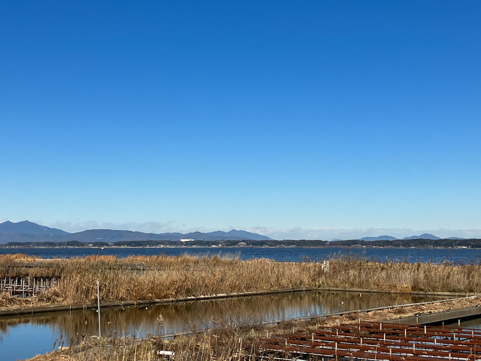 Landschaft mit blauem Himmel, Wasserfläche, fernen Bergen und trockenem Gras