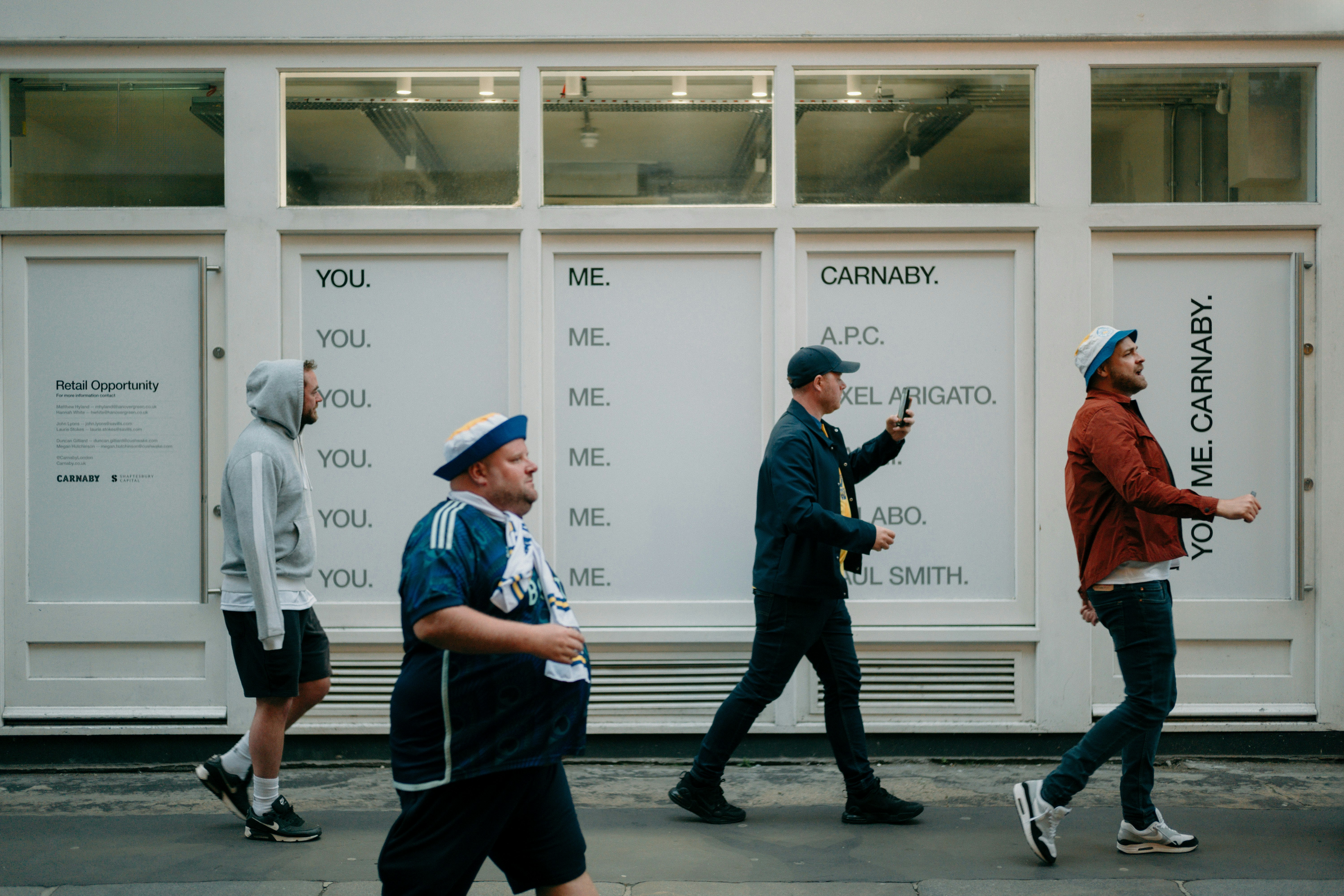 Persone che camminano davanti a un muro bianco con grandi annunci tipografici