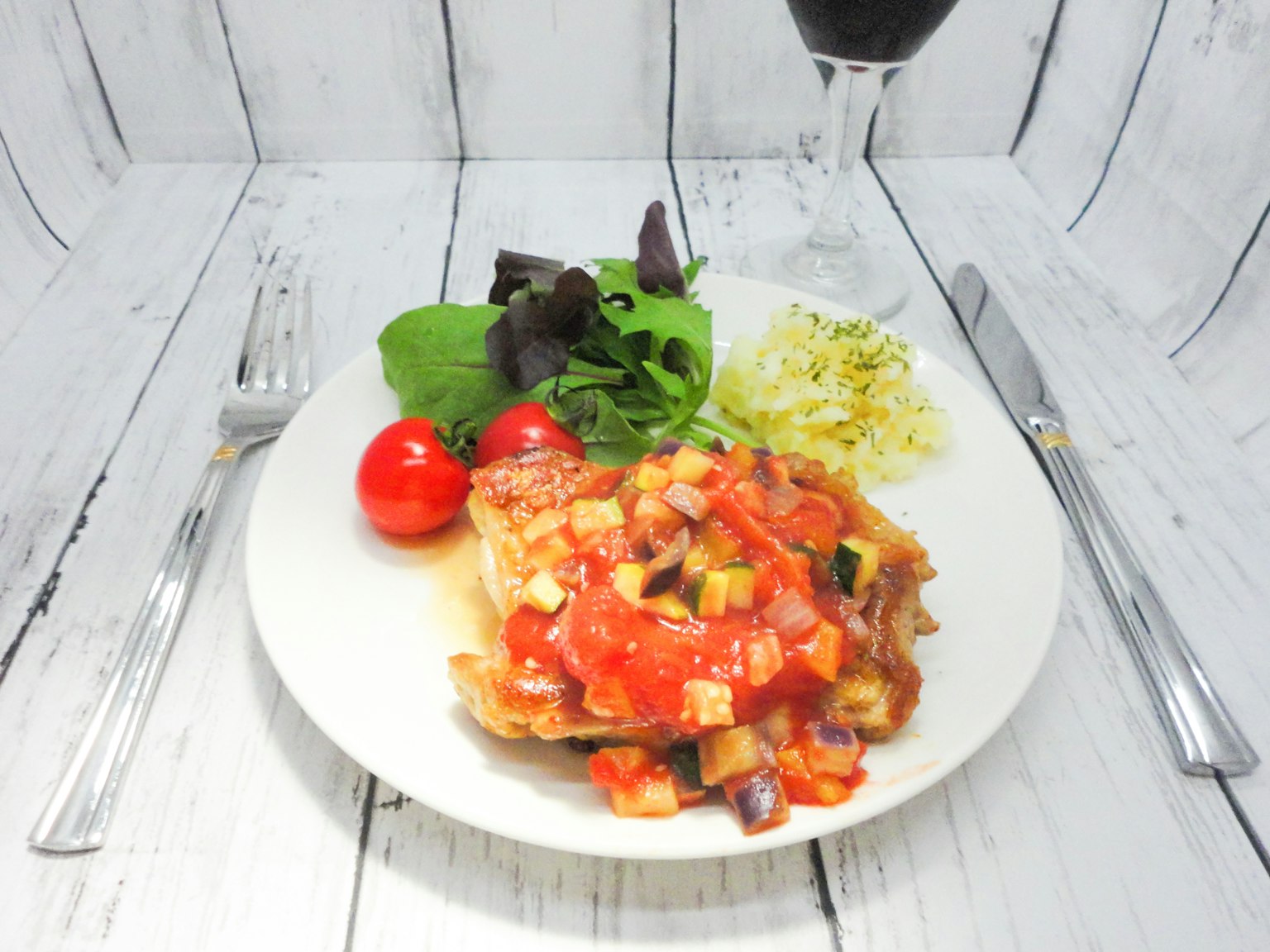 Gericht mit Tomatensauce auf einem weißen Teller, serviert mit Salat und Kirschtomaten