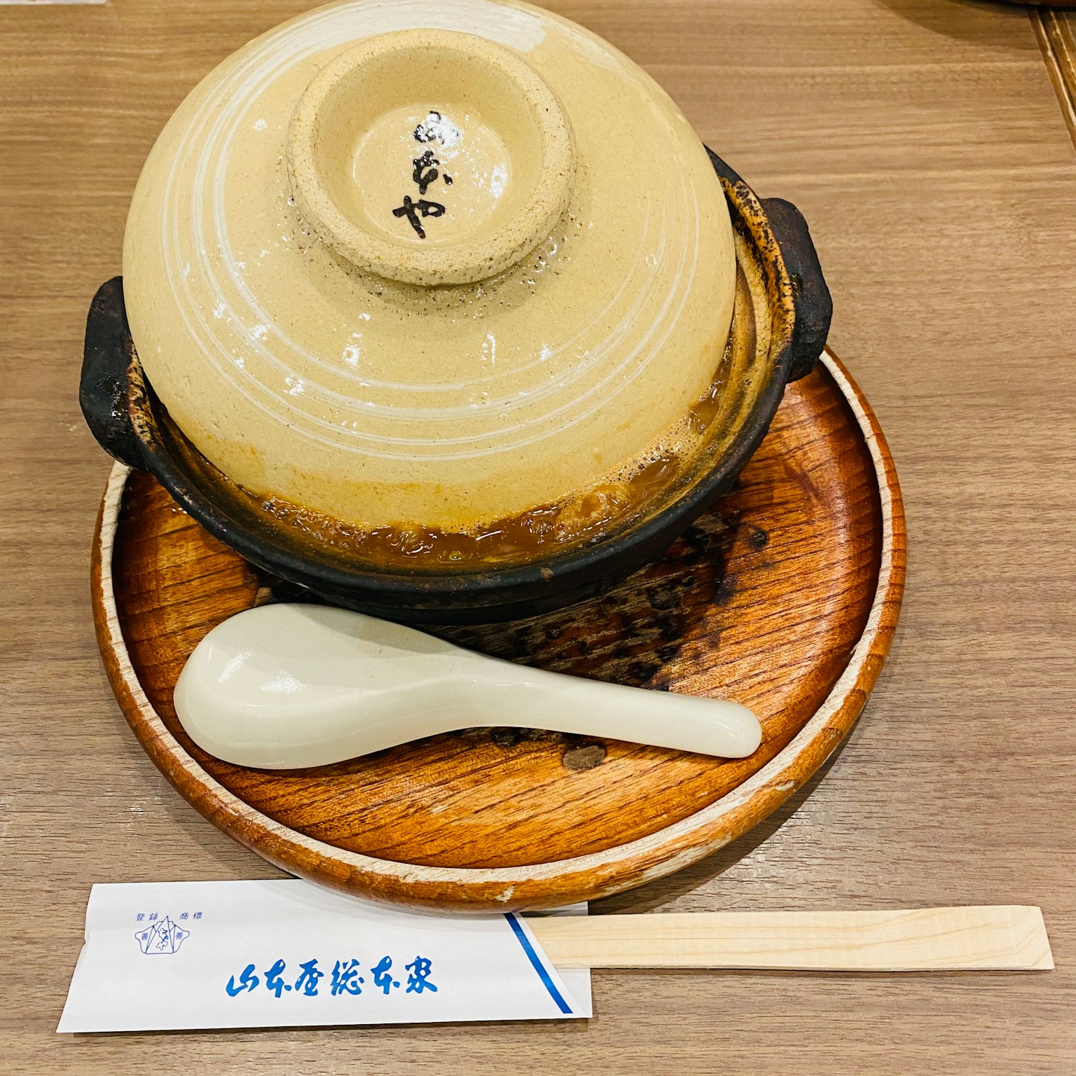 一个放在木托盘上的陶瓷锅，旁边有勺子和筷子