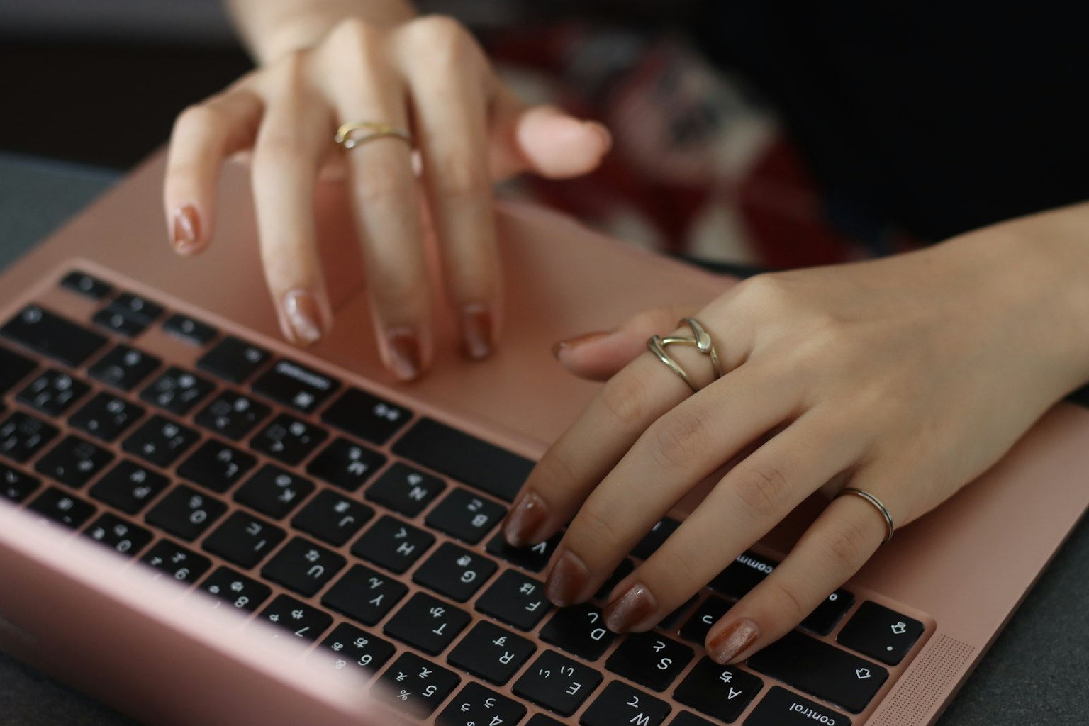 Primer plano de manos escribiendo en un teclado rosa con múltiples anillos