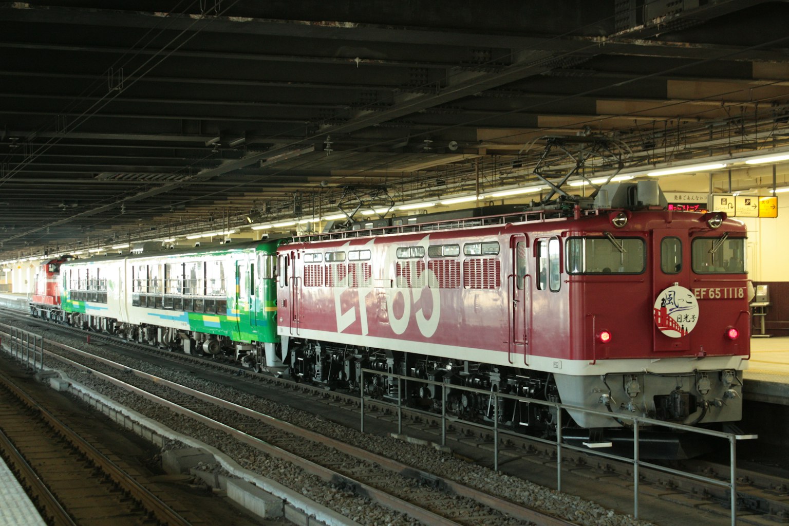 Locomotiva rossa con carrozze passeggeri verdi in una stazione