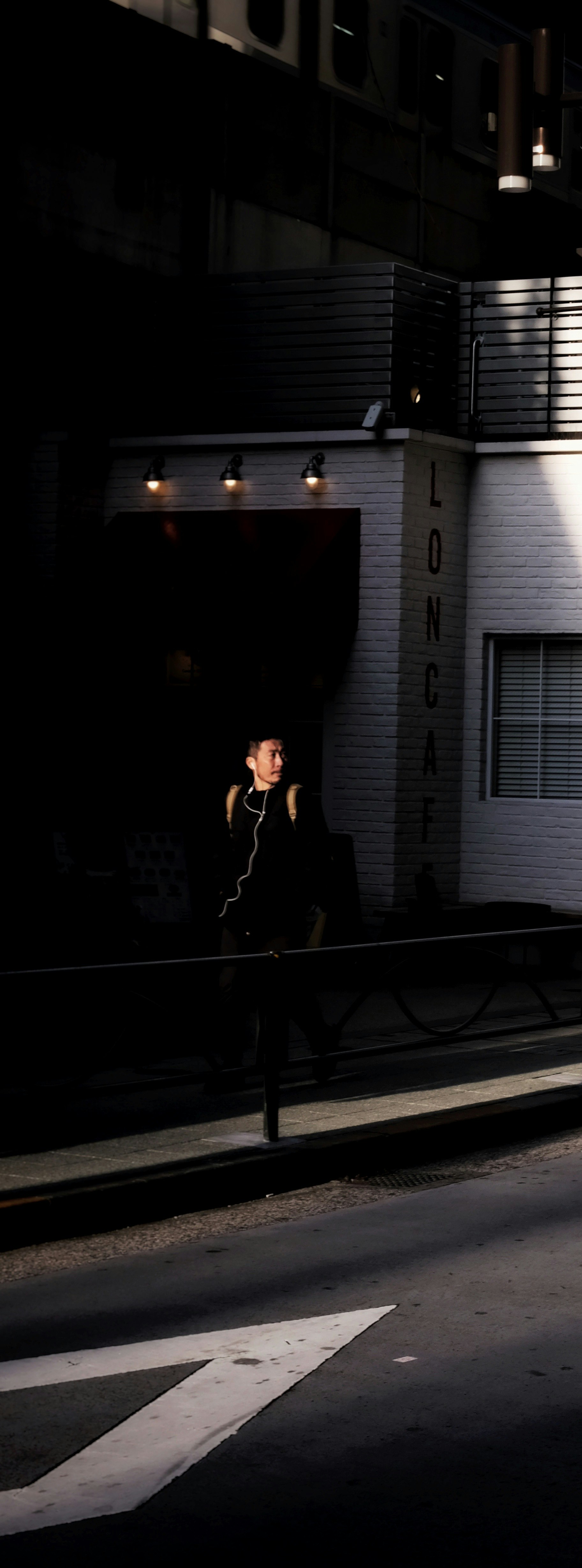eine Person, die durch tiefe Schatten und starkes Sonnenlicht in einer Gasse geht