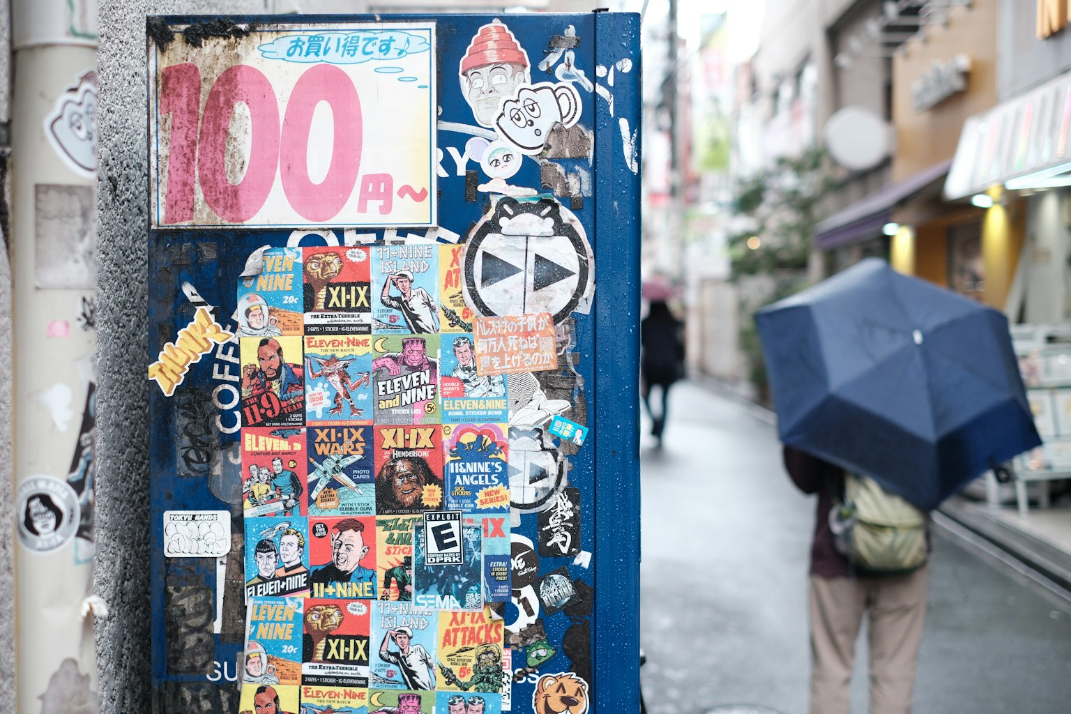 Enge Gasse mit einer blauen Wand, die mit bunten Aufklebern bedeckt ist, und einem Schild mit der Aufschrift 100 Yen