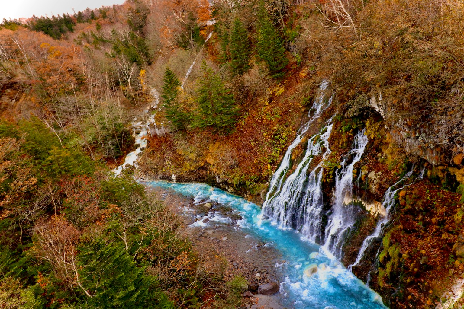 Vista escénica de una cascada que fluye hacia un río azul rodeado de follaje otoñal