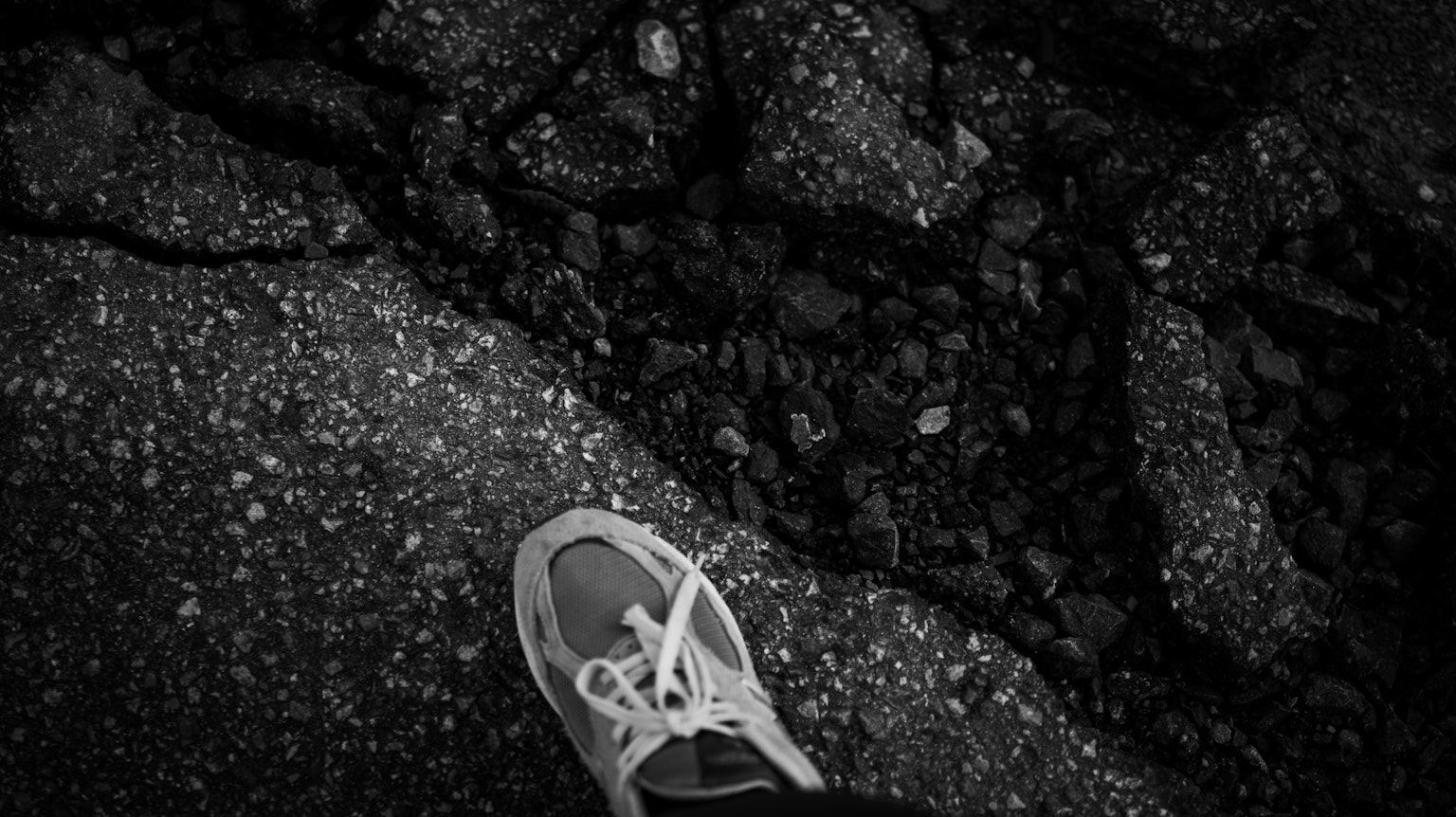 Acercamiento a una zapatilla sobre pavimento agrietado en blanco y negro