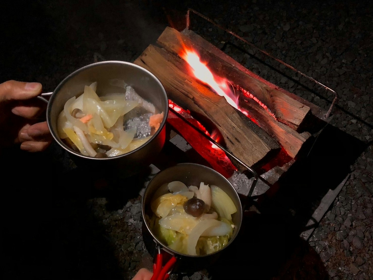 Dua panci yang dimasak di atas api unggun di malam hari