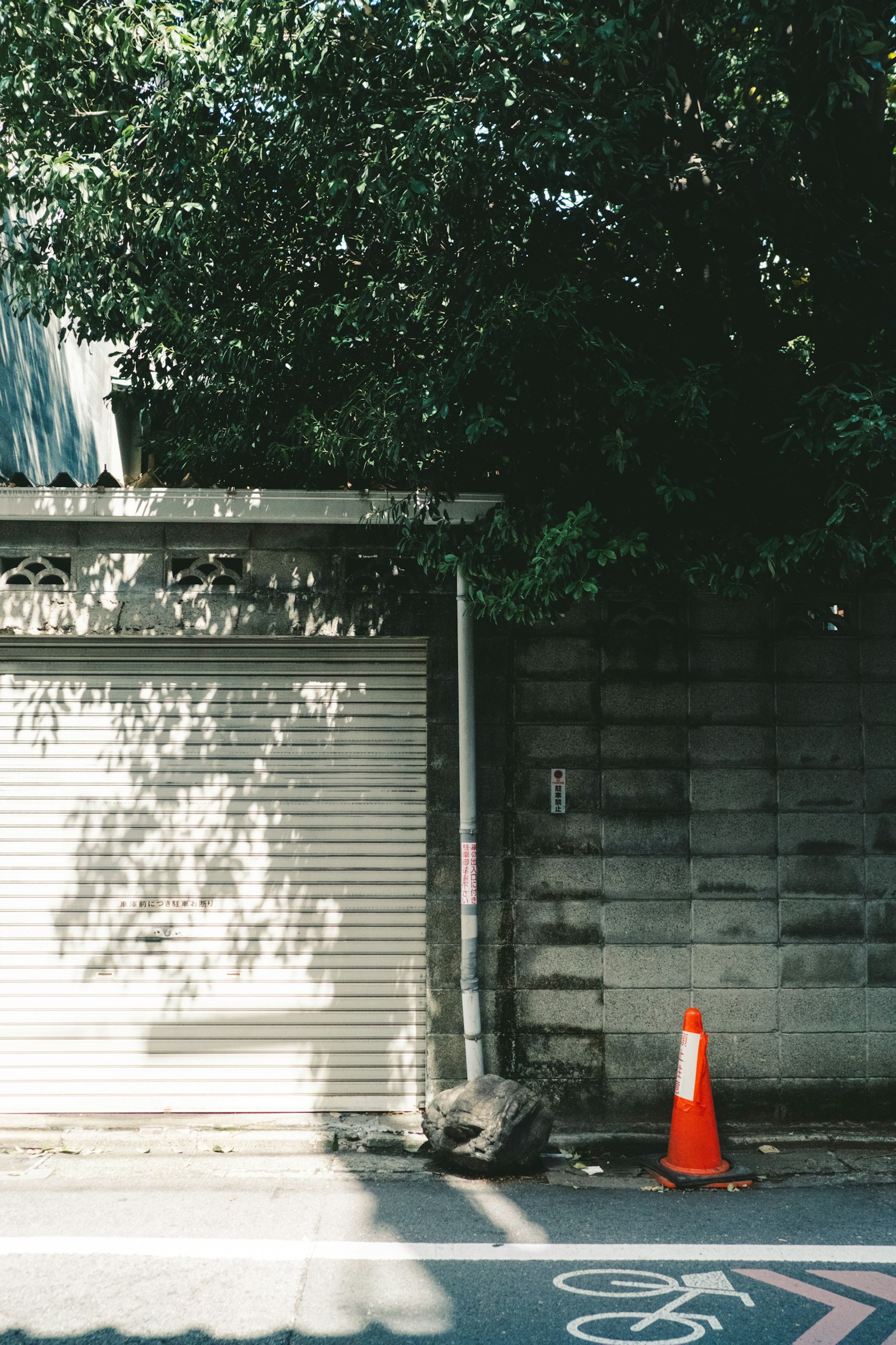 Quiet street scene featuring an orange traffic cone and a shuttered shop