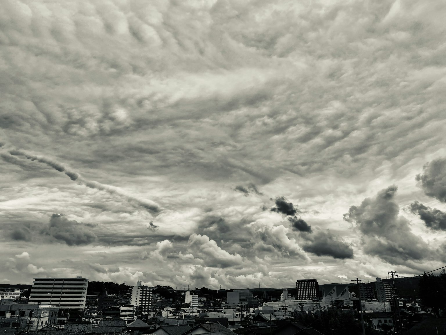 Foto monokrom langit dipenuhi awan di atas lanskap perkotaan