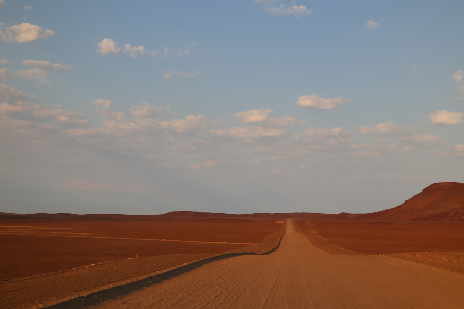Camino solitario a través de un vasto desierto rojo bajo un cielo azul