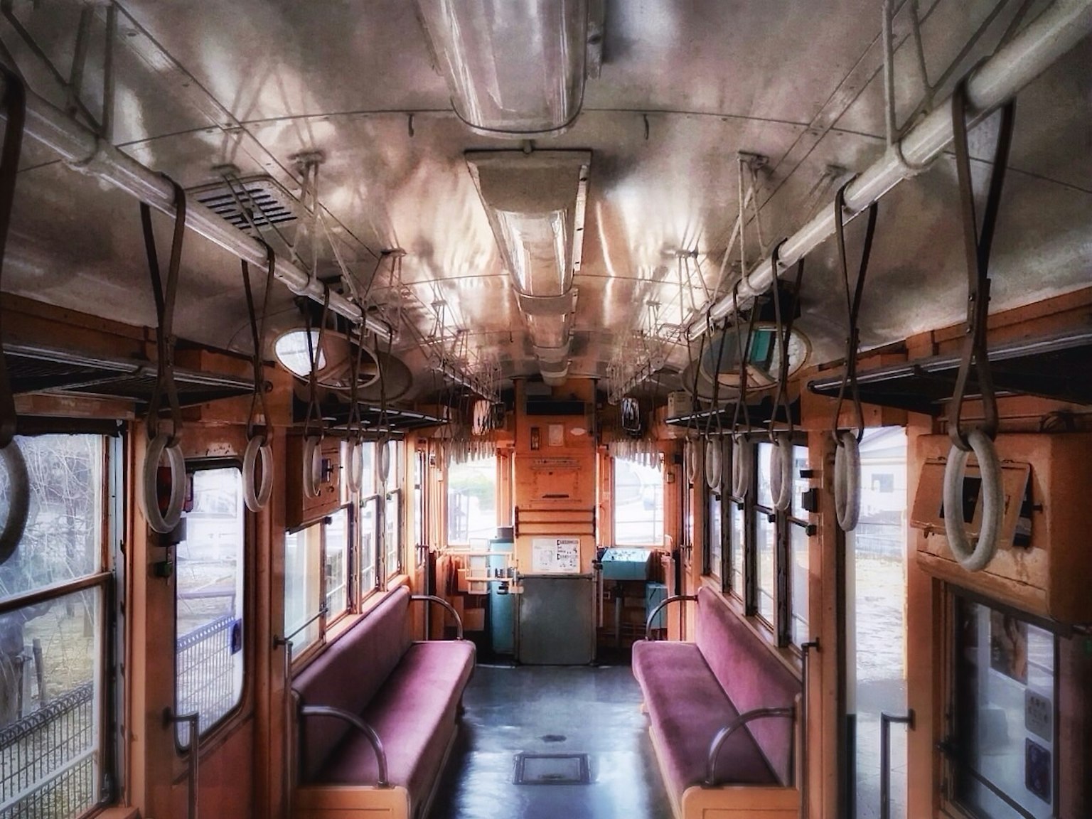 Interior de un tren antiguo con bancos de madera y asas colgantes
