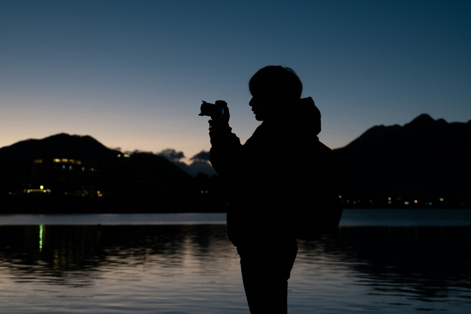 黄昏时分在湖边拿着相机的人影