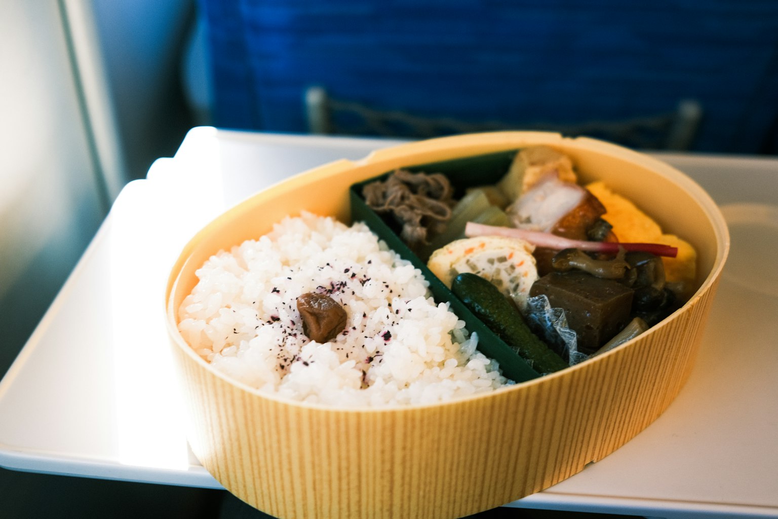 Photo d'une boîte à bento servie dans un avion avec du riz et divers plats d'accompagnement disposés dans un contenant en bambou