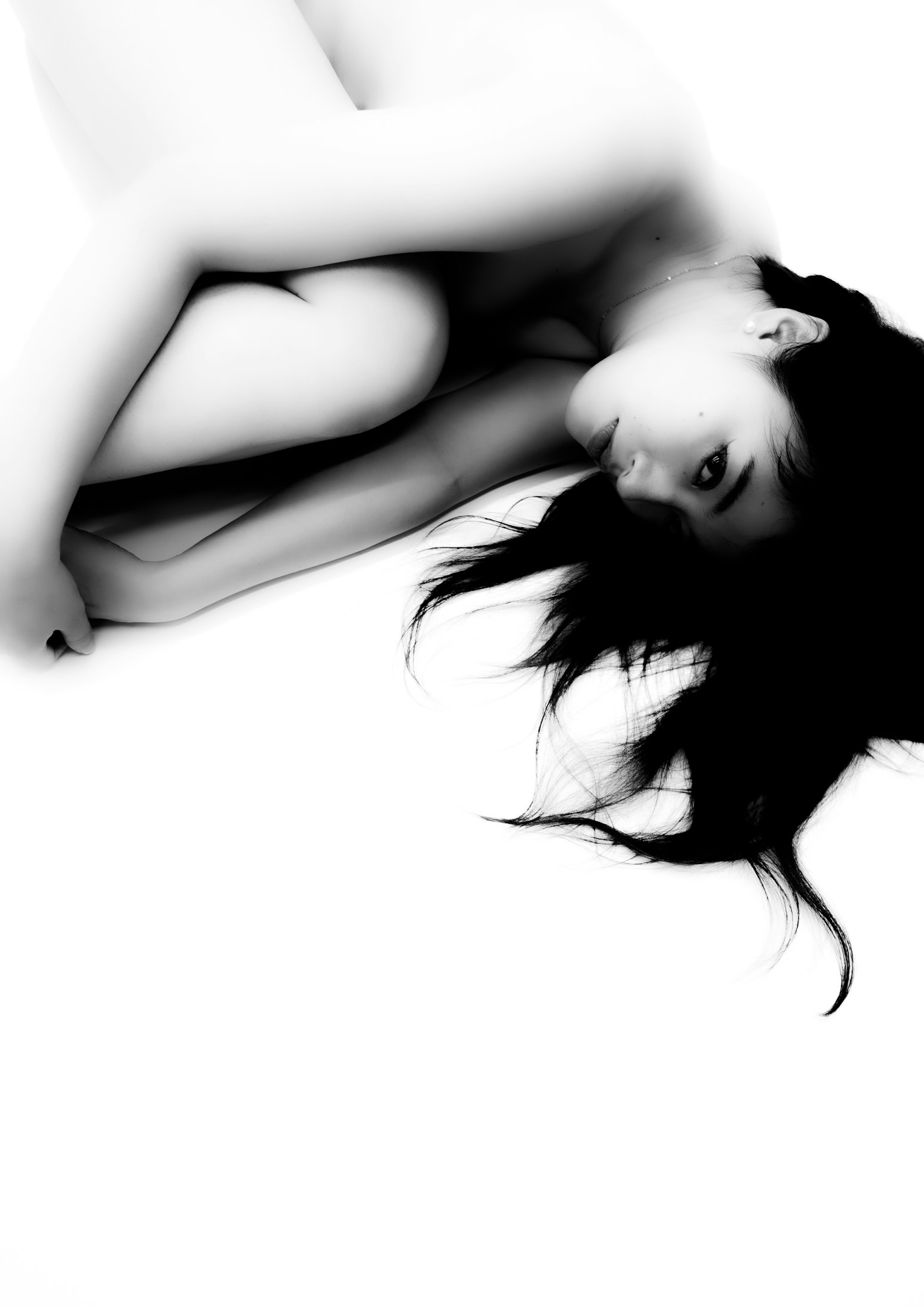 白黒のアート写真で、女性が体を丸めている姿が描かれている