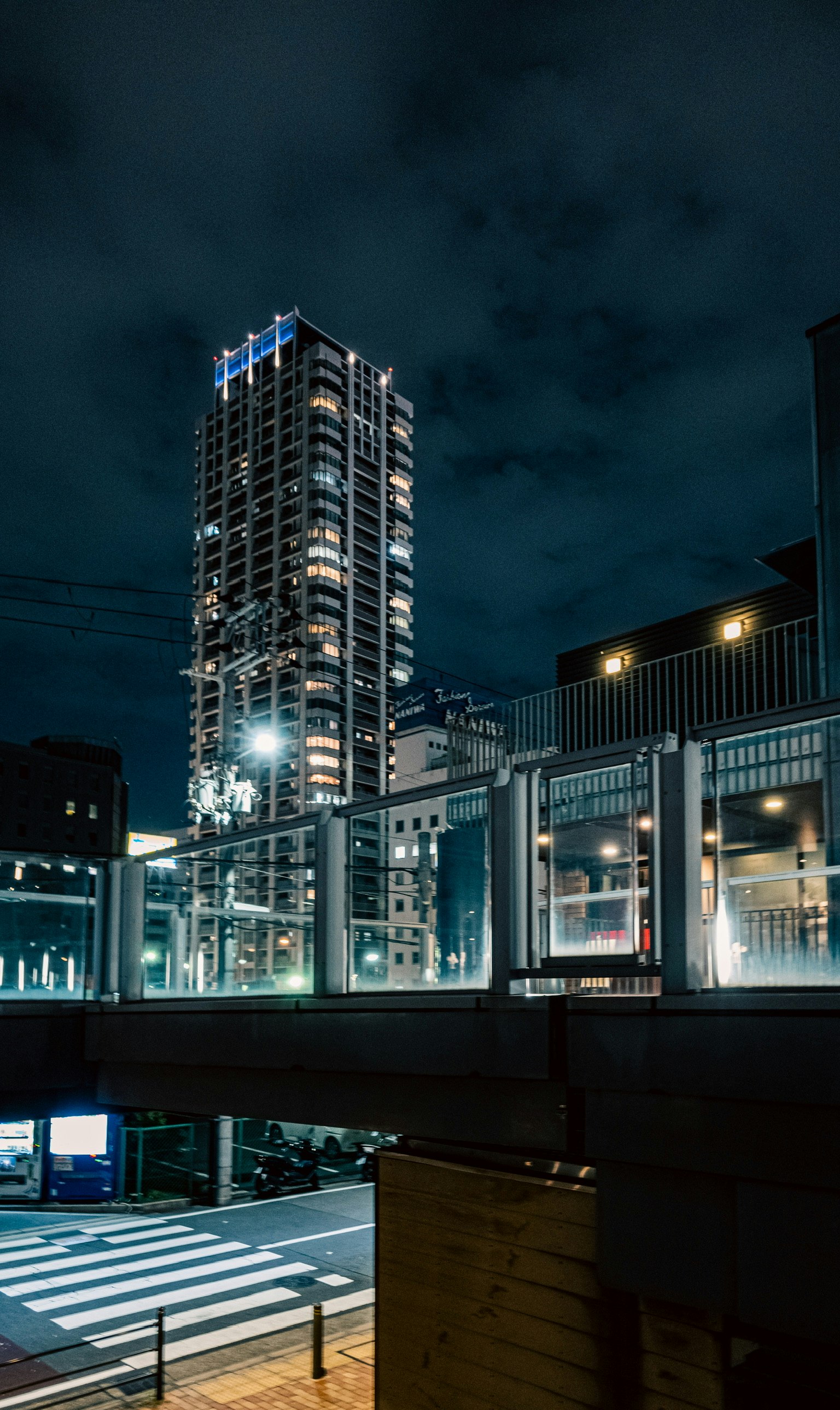 Night cityscape featuring a tall building and pedestrian bridge