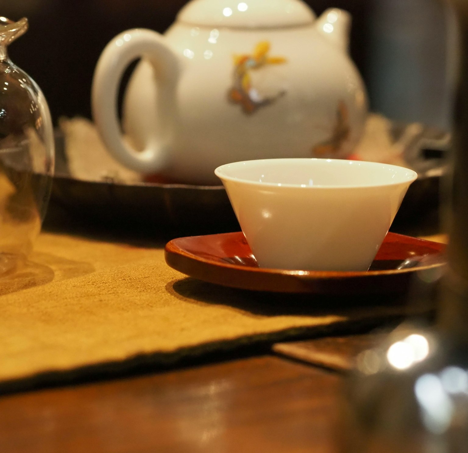 Eine weiße Teetasse auf einer roten Untertasse neben einer Teekanne auf einem Holztisch