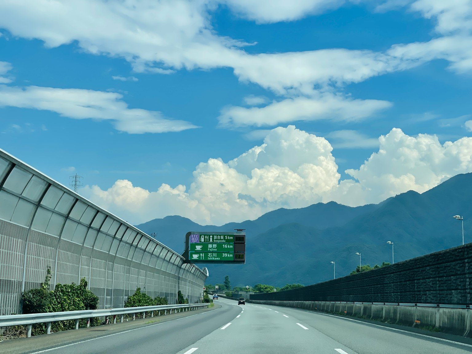 Vue panoramique d'une autoroute avec ciel bleu et nuages blancs montagnes en arrière-plan panneau routier visible