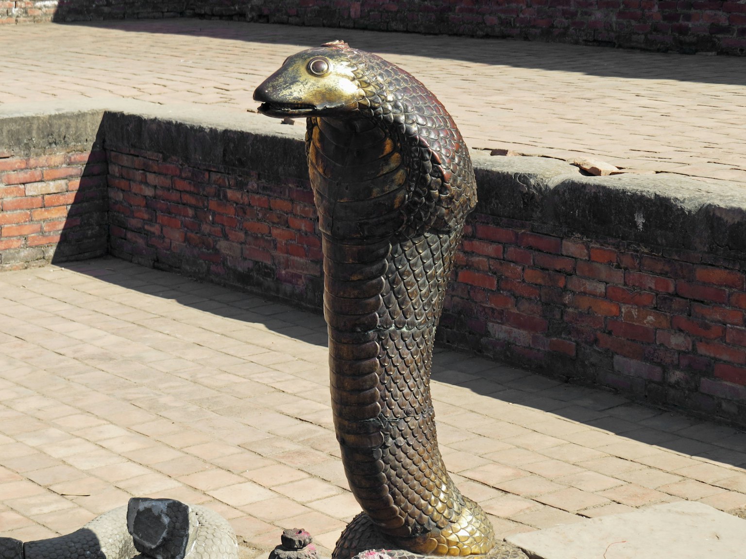 Une statue de cobra doré se tenant sur une plateforme en pierre avec un fond en brique