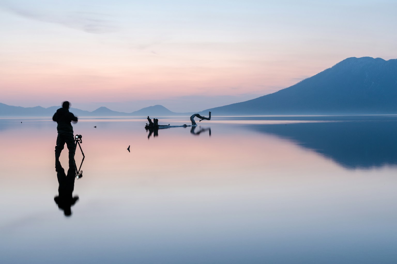 Silhouette d'une personne prenant des photos au bord d'un lac tranquille avec un magnifique lever de soleil