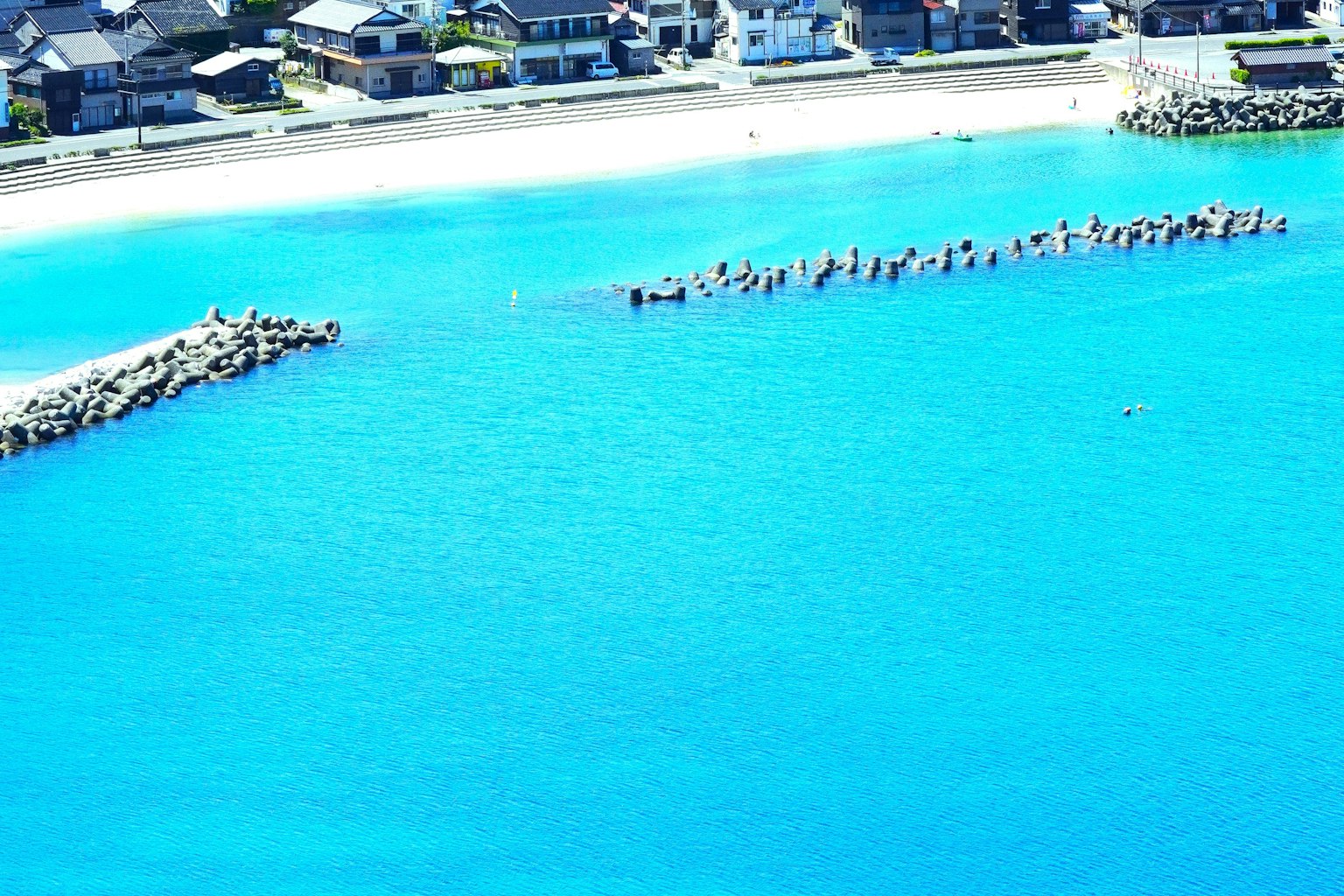 Vista panoramica dell'acqua blu brillante e della spiaggia sabbiosa con formazioni di frangiflutti