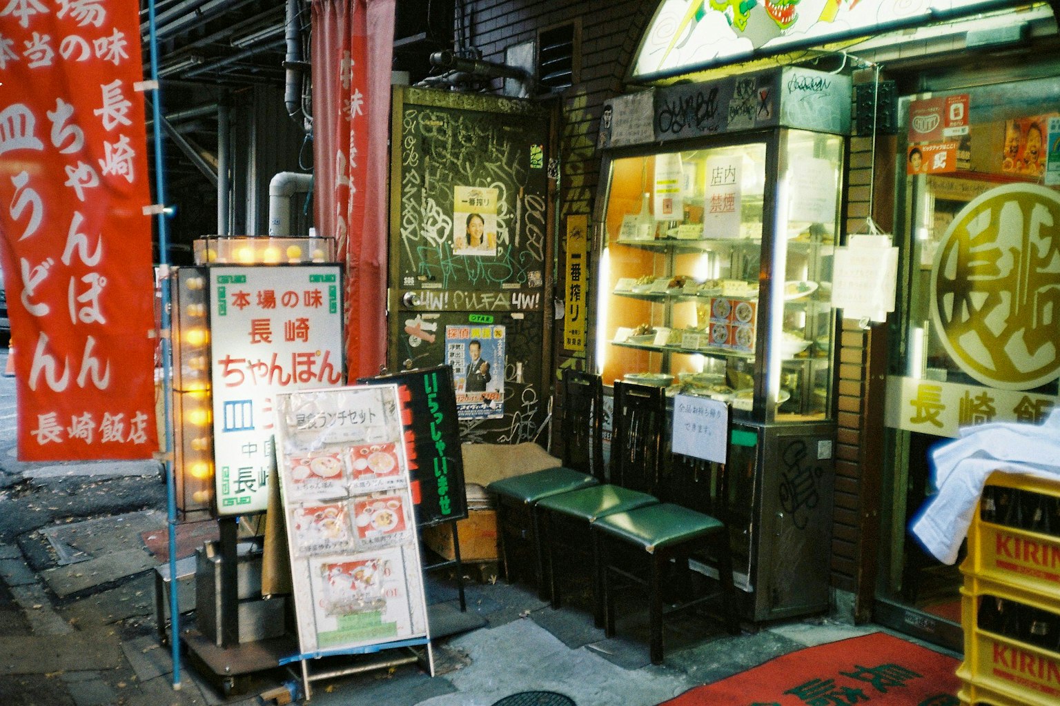 Exterior of a Japanese udon shop in a narrow alley with a menu sign and seating outside