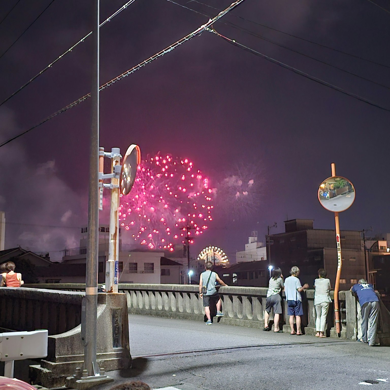 Fireworks blooming in the night sky with spectators on a bridge