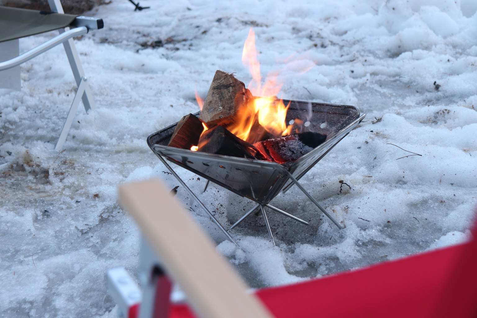 Un feu de camp brûlant sur la neige avec des chaises de camping à proximité