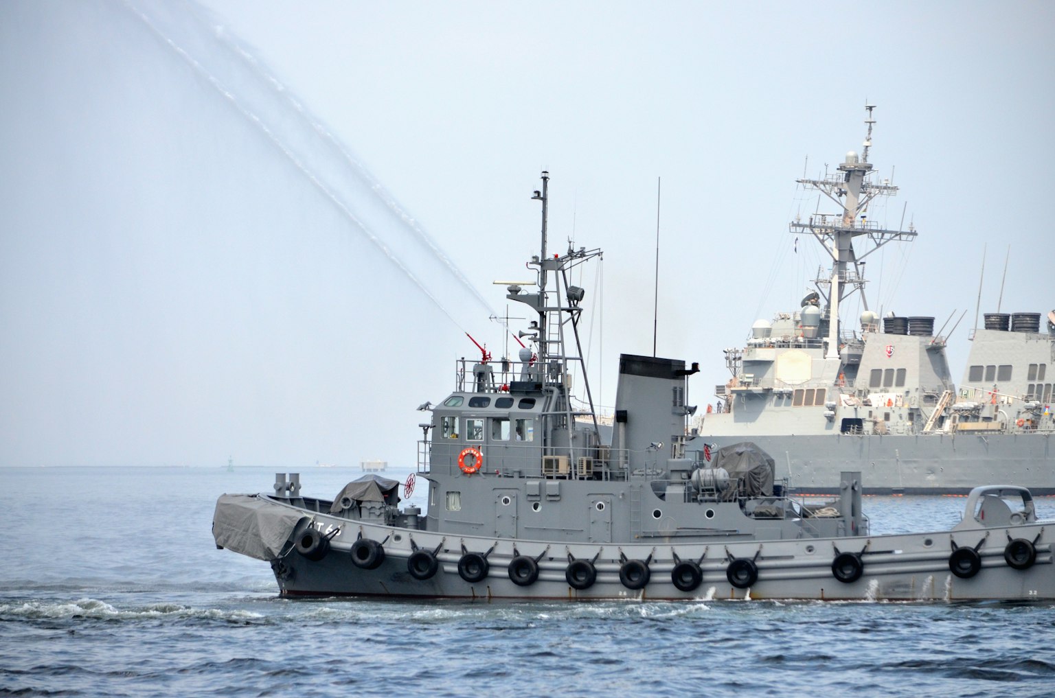 Bild eines kleinen Arbeitsboots neben einem großen Kriegsschiff auf dem Wasser