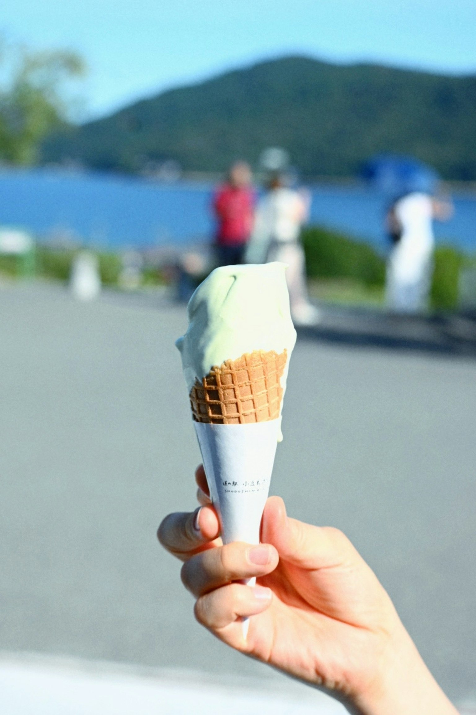 手に持たれた緑色のアイスクリームコーンと背景の湖