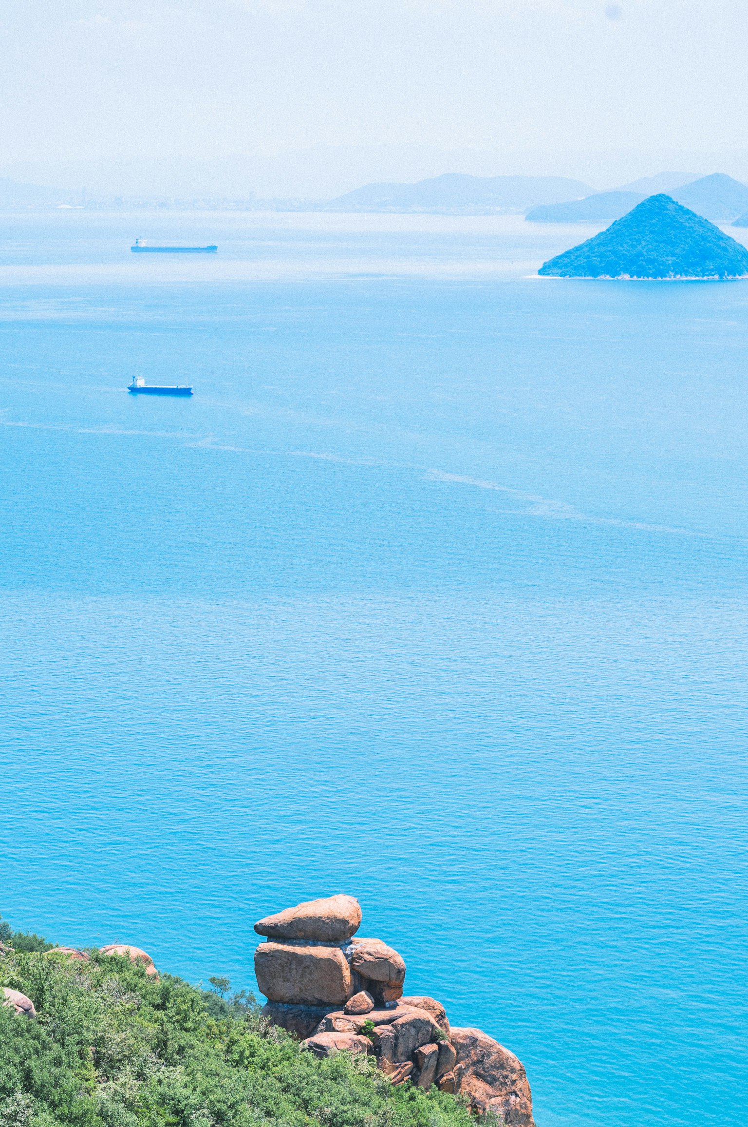 Vista panoramica dell'oceano blu con isole lontane e un grande masso in primo piano