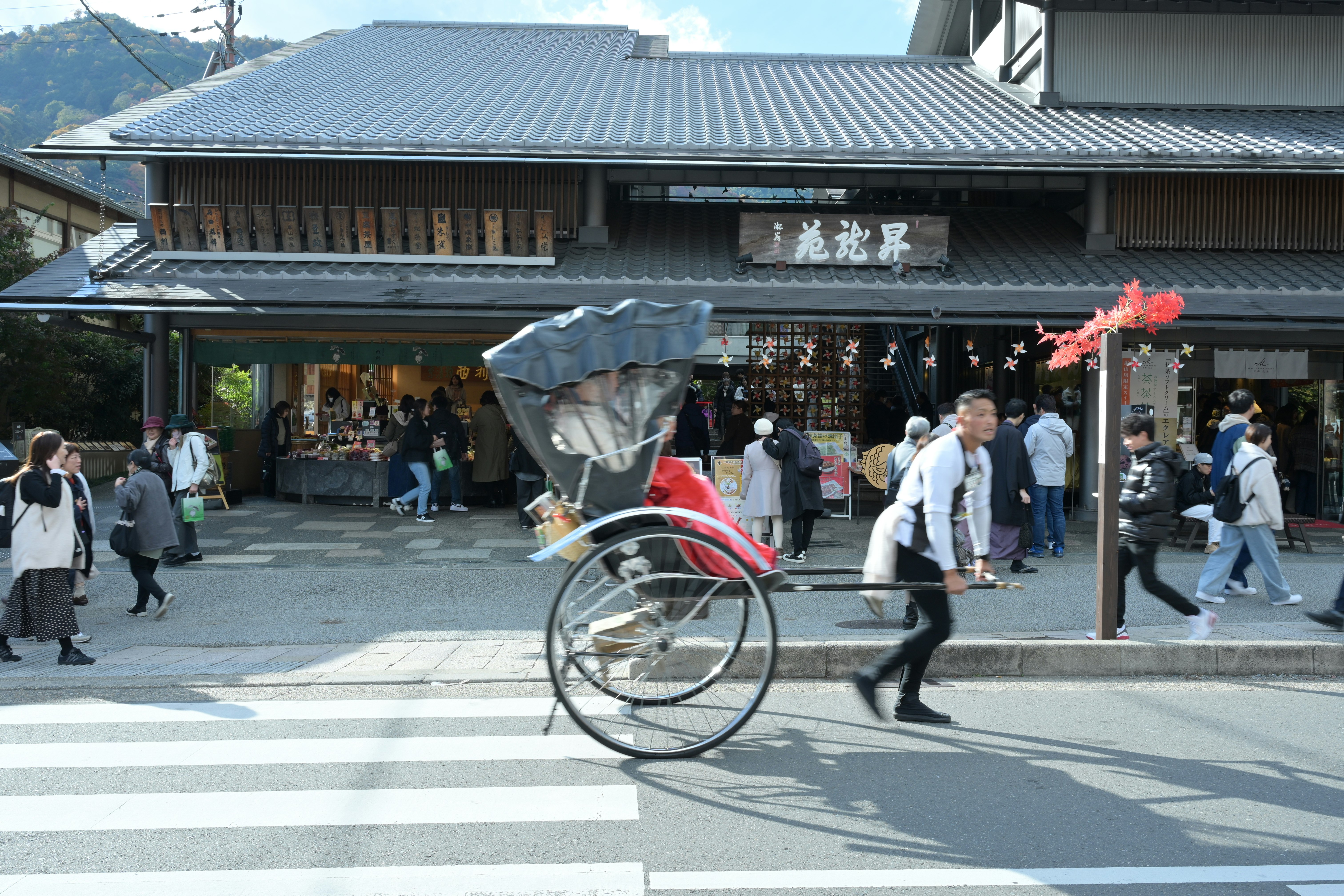山並みを背景にした和風の駅前通りで人と自転車が行き交う