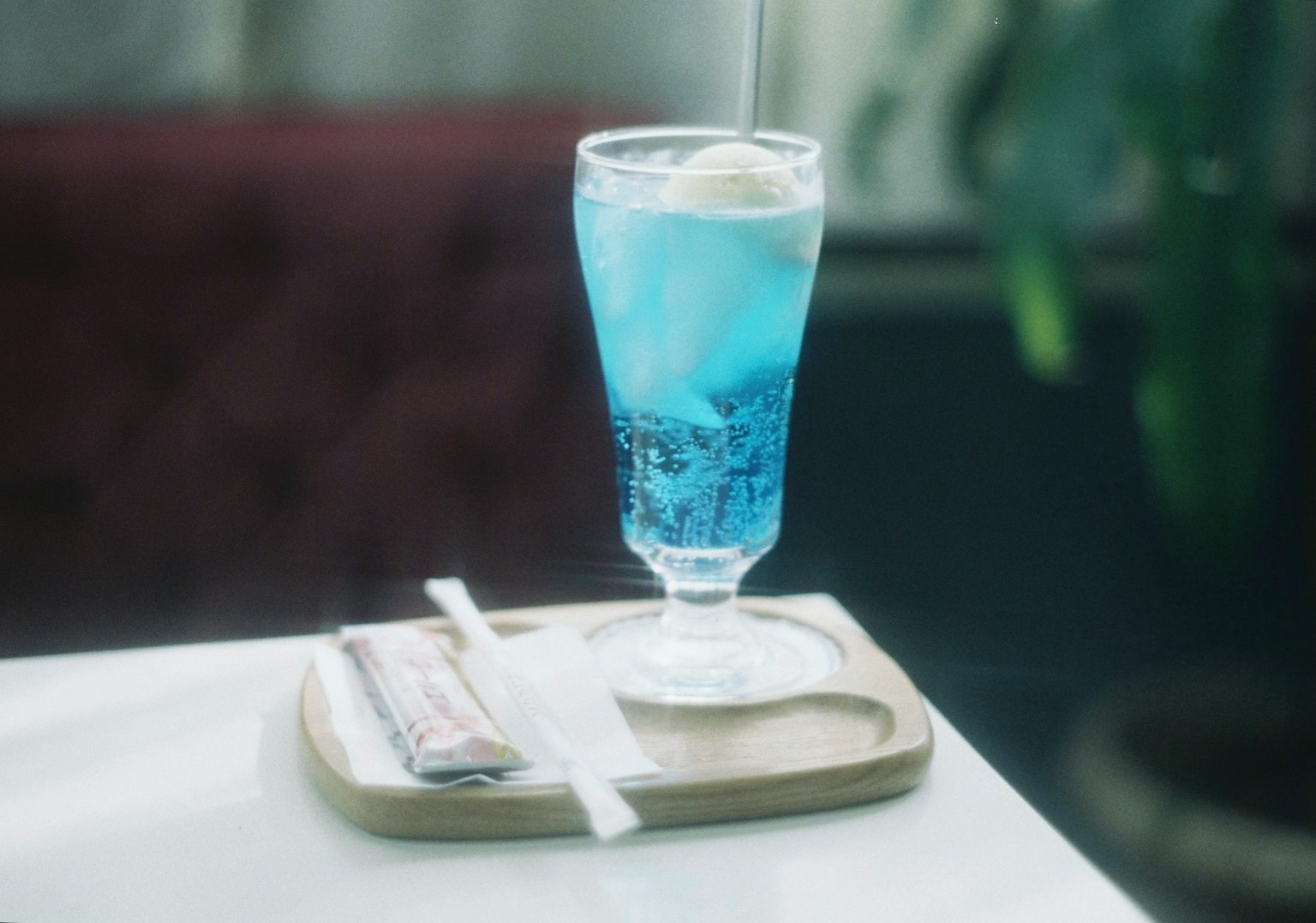 Un bicchiere di bevanda blu con gelato sopra posato su un vassoio di legno