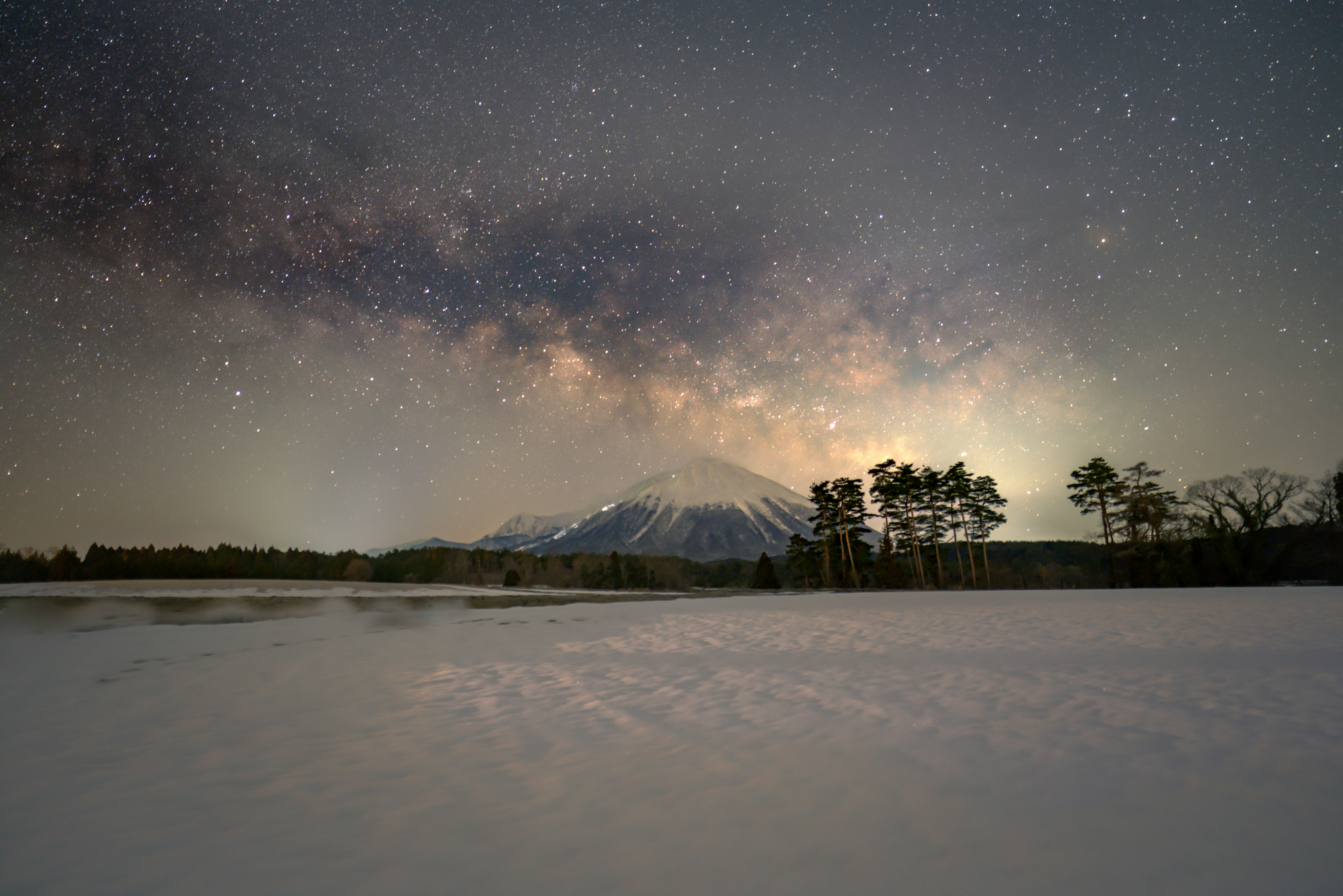 雪原に広がる天の川と星空、遠くの山並み