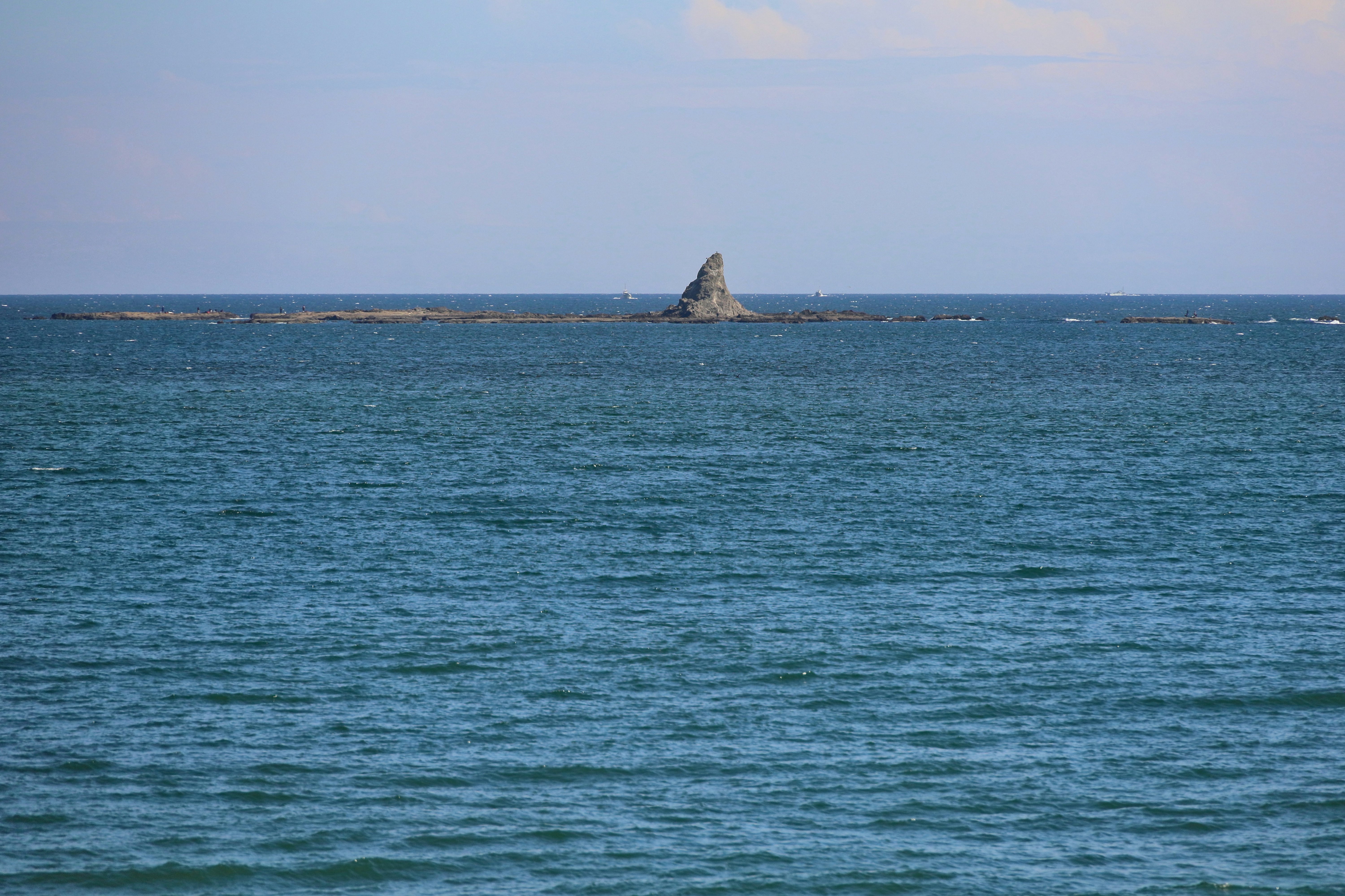 水平線に浮かぶ青い海と岩の岬の景色