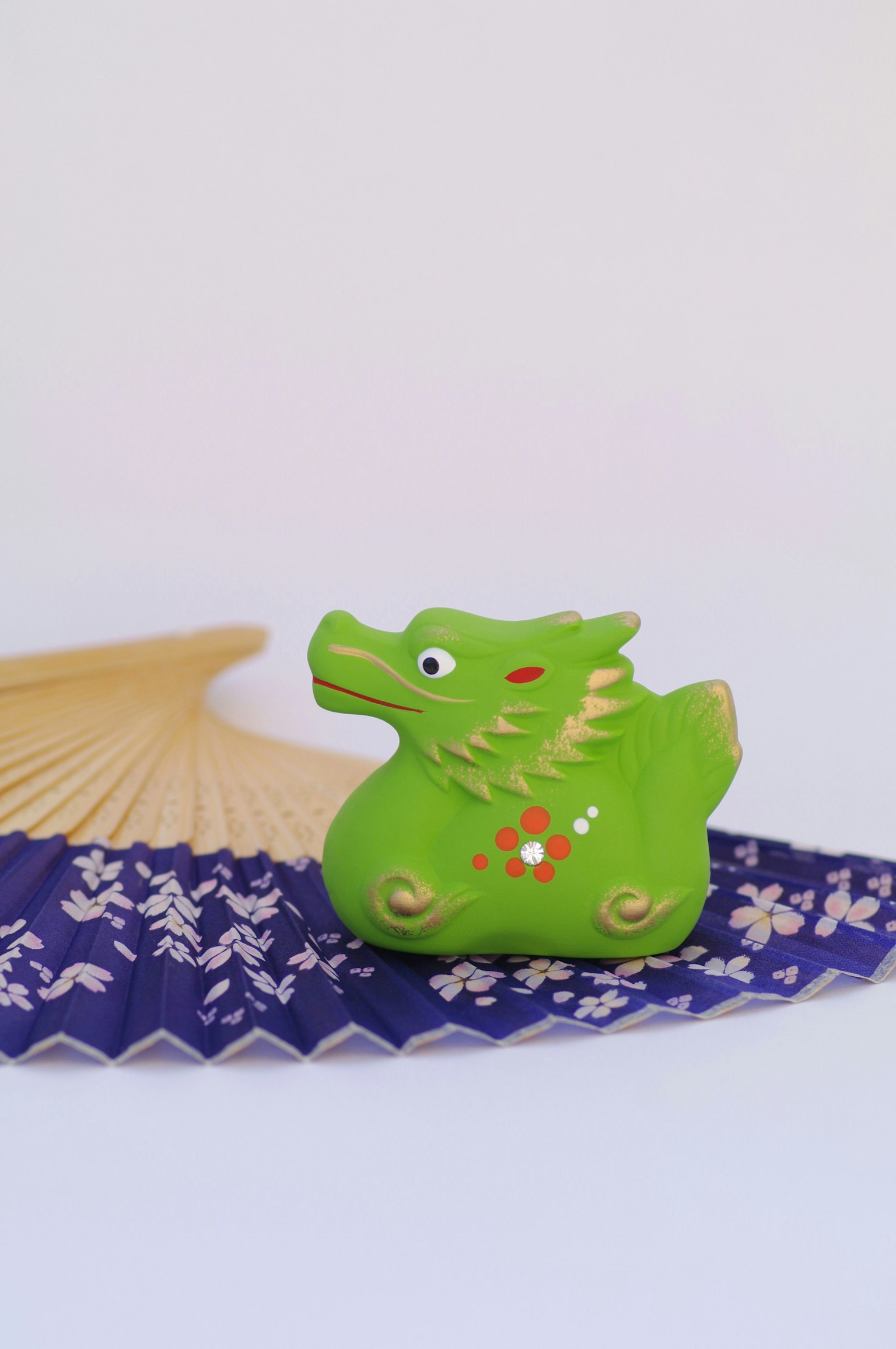 Una figura en forma de dragón verde junto a un abanico morado