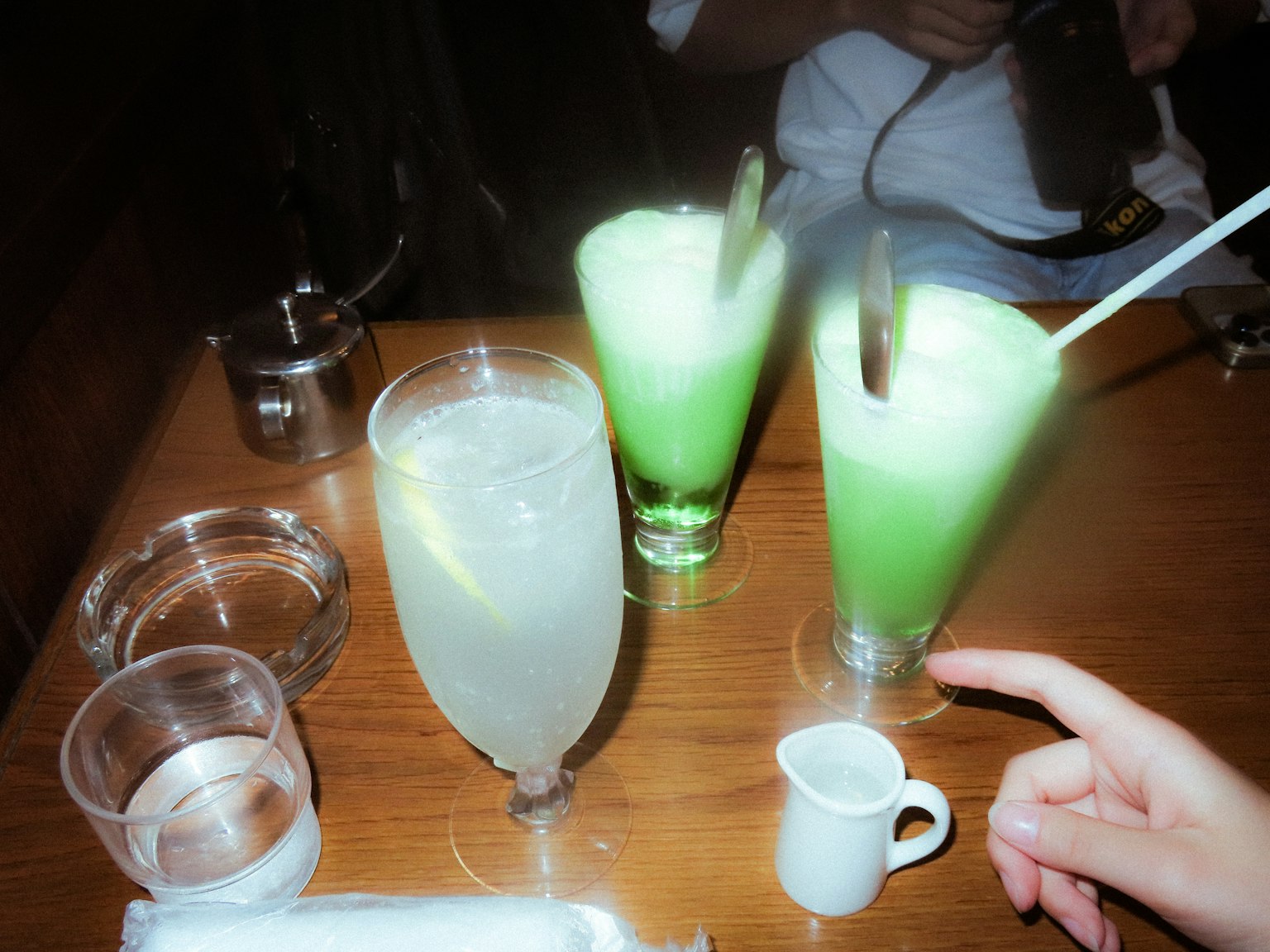 Bicchieri di bevande verdi e chiare su un tavolo di legno con una mano che si avvicina
